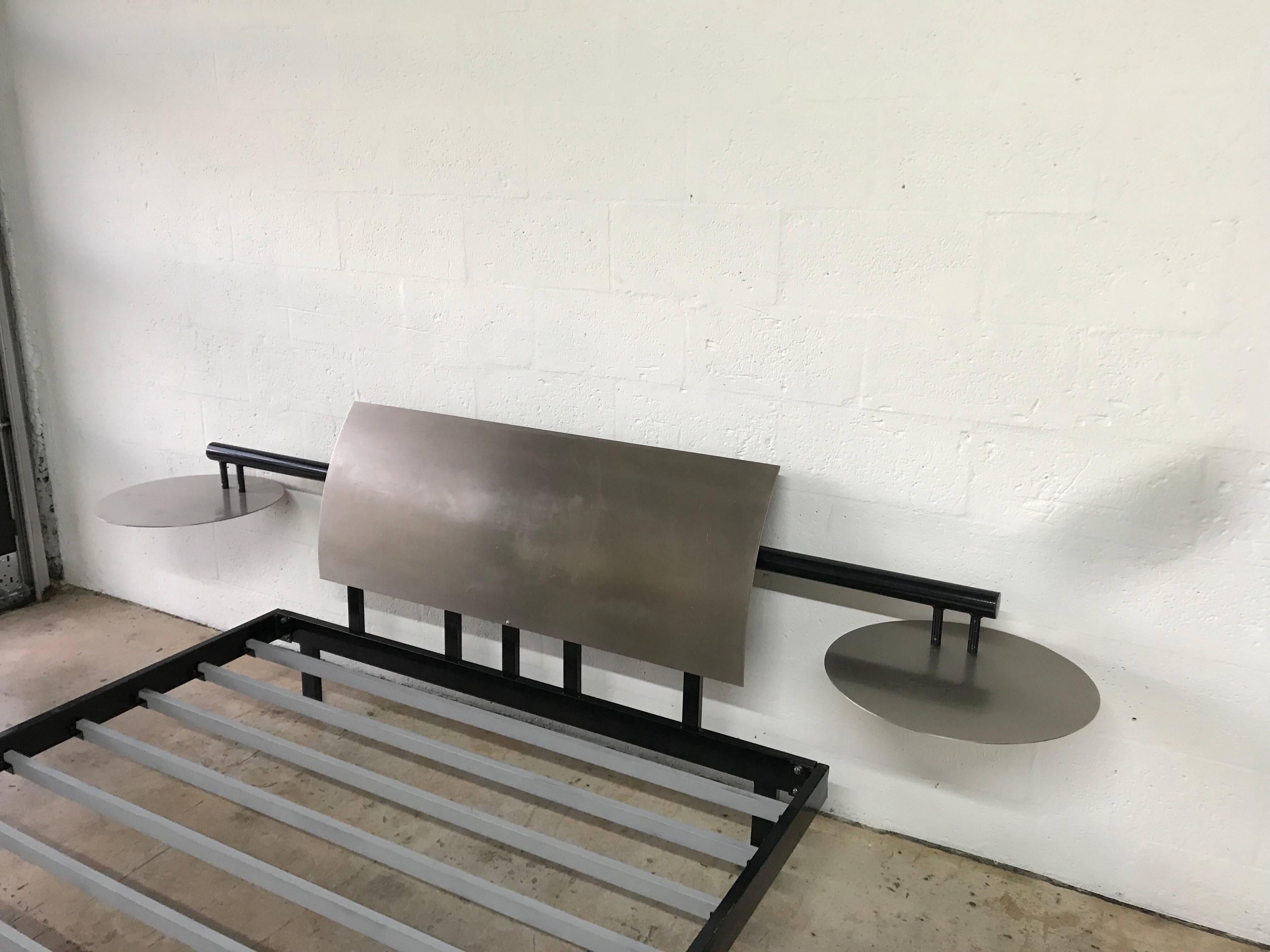Postmodern enameled steel bed frame with a curved stainless steel headboard and integrated floating stainless steel nightstands, circa 1980s.

Additional dimensions:
Bed frame-
62” wide
10” high
Rails-
9” high
Nightstands-
19” diameter
21.5” high.
 