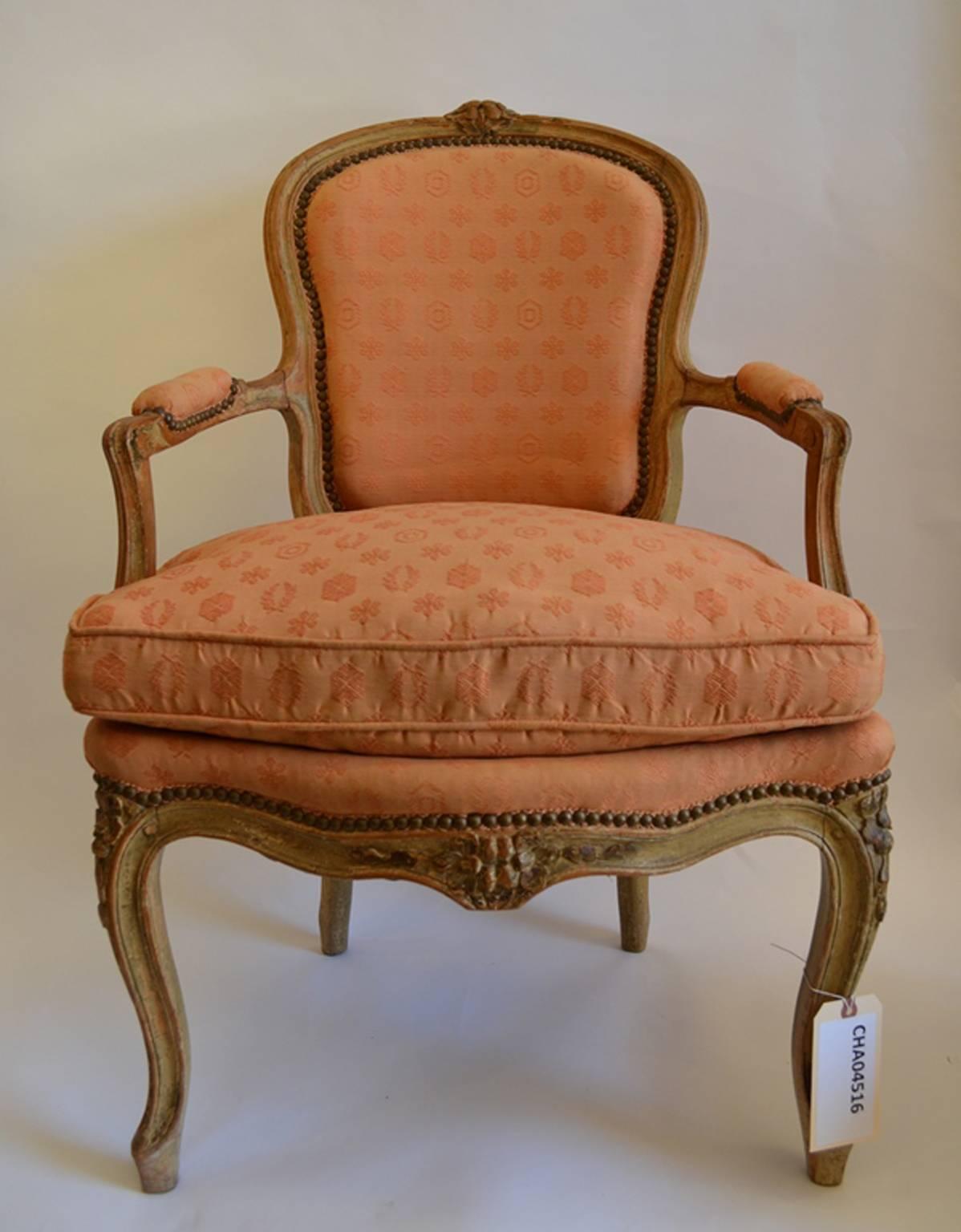 A pair of Louis XV carved and Crème Peinte Fauteuils, 18th century, rounded floral crests, padded arms, serpentine seat rail, floral cabriole legs. Upholstered in a period Salmon colored Damask.