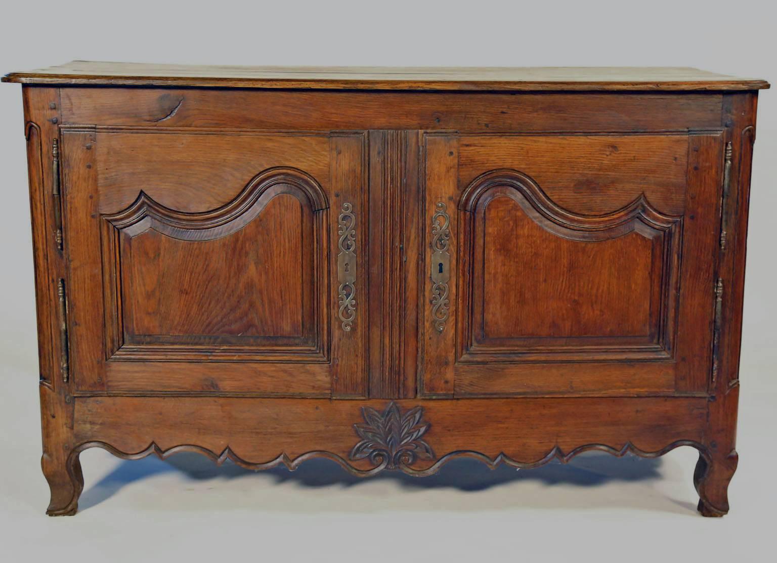 19th century buffet with beautiful plank top with a beveled edge, over two carved and molded paneled doors. Paneled Doors have Double hinges and an ornamental key plate over a scalloped and molded apron with a central carved stylized Flower, resting
