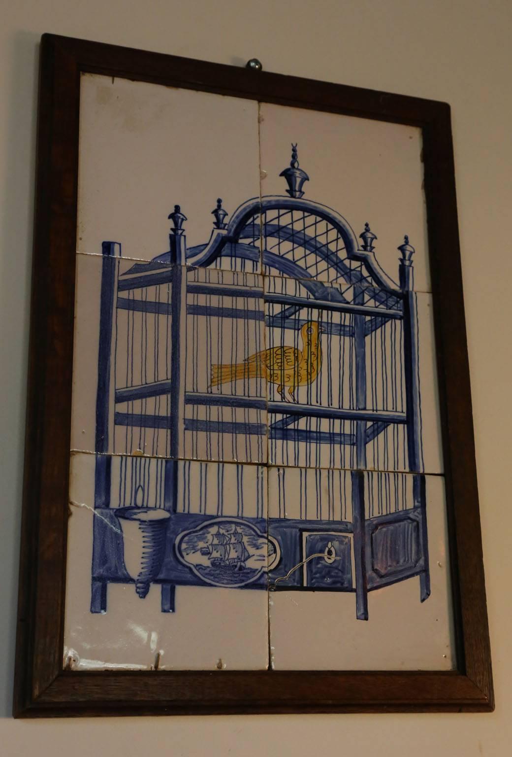 19th century Delft tile wall picture of a bird in a cage with the typical blue color used in Delft tiles, with a painted yellow bird and a central ship on the cage.