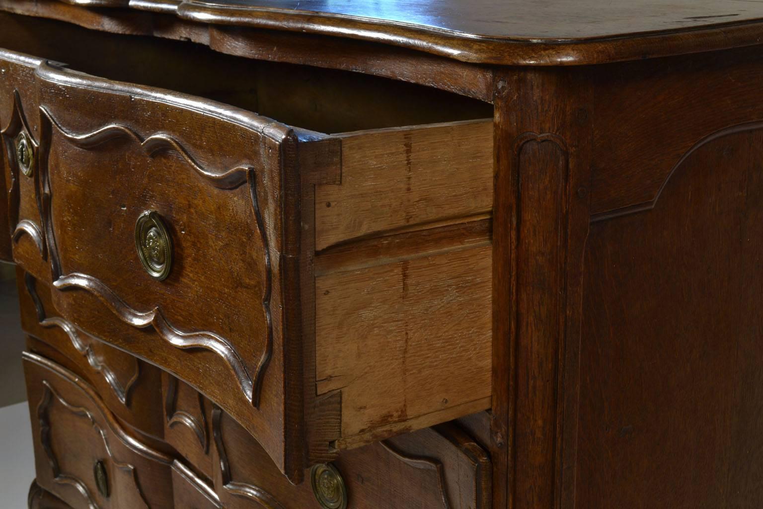 A French provincial carved oak commode, 18th century, serpentine top, the blocked case with three drawers, panelled chamfered stiles, C-scrolled apron centred by a shell, and cabriole legs.