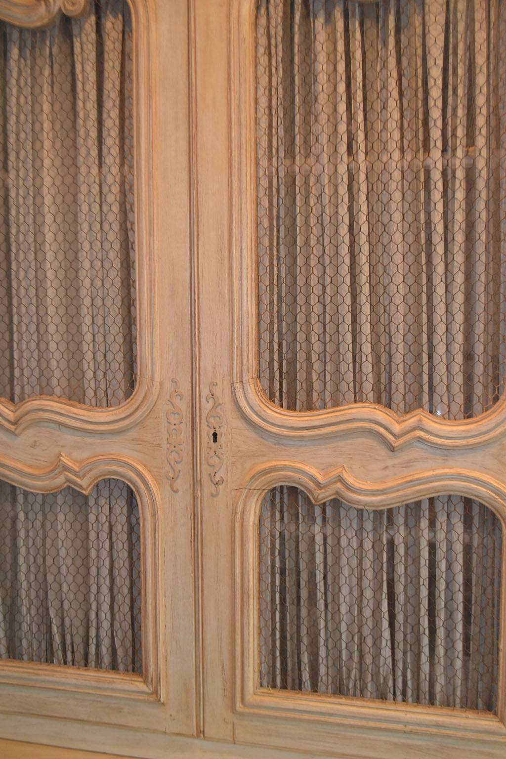 French, Provincial, painted cabinet; the molded cornice above a cabinet fitted with four doors, each fabric-backed and fitted with two wire grill panels, the lower section fitted with four doors, each inset with a shaped, molded panel, raised on a