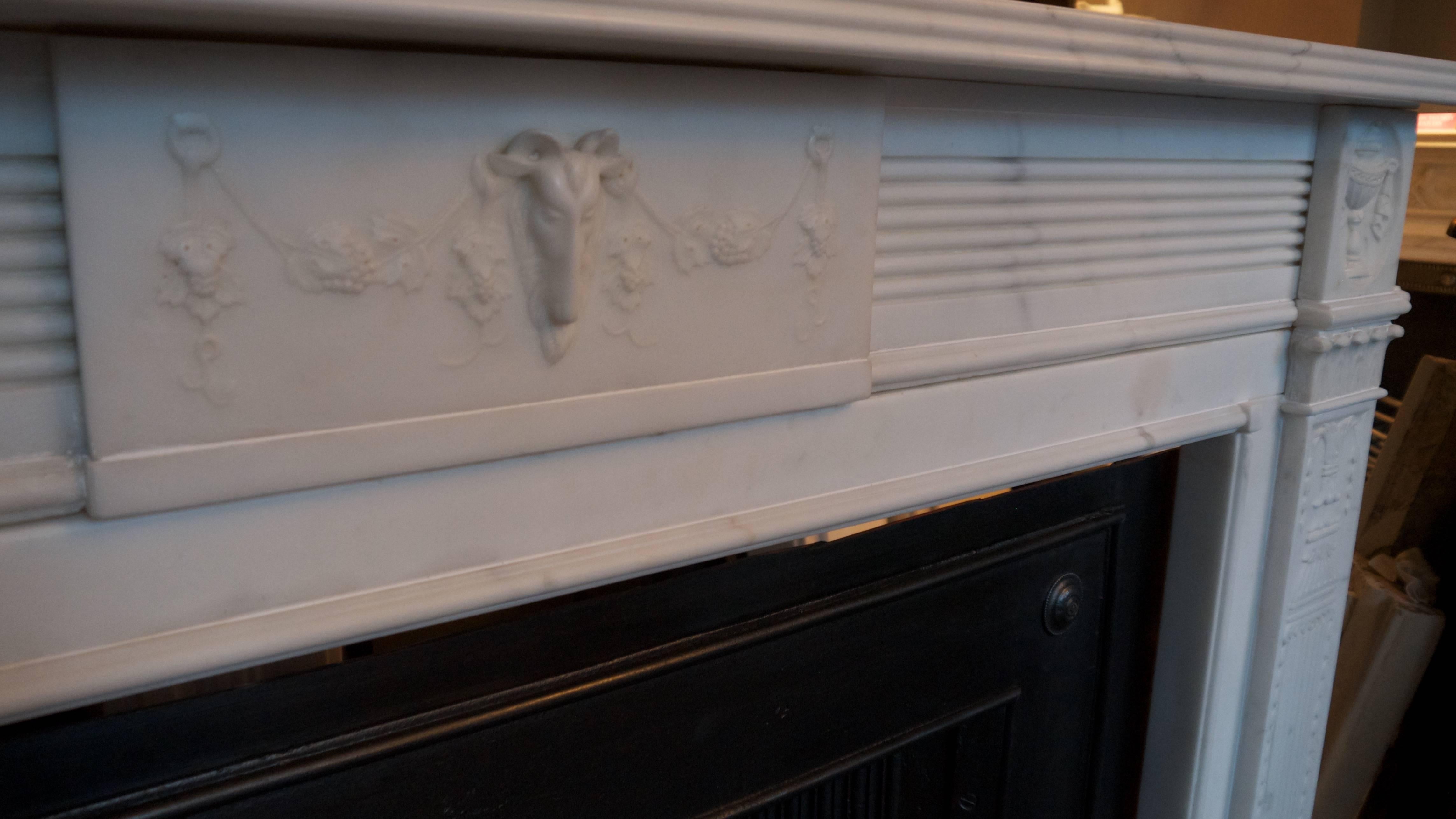 Irish antique Georgian Statuary white marble fireplace with tapering fluted pilasters, ribbon tied urn corner blocks. A reeded frieze and a centre tablet featuring a goats mask with grape vine swags and a double reeded shelf. Opening size 43.25