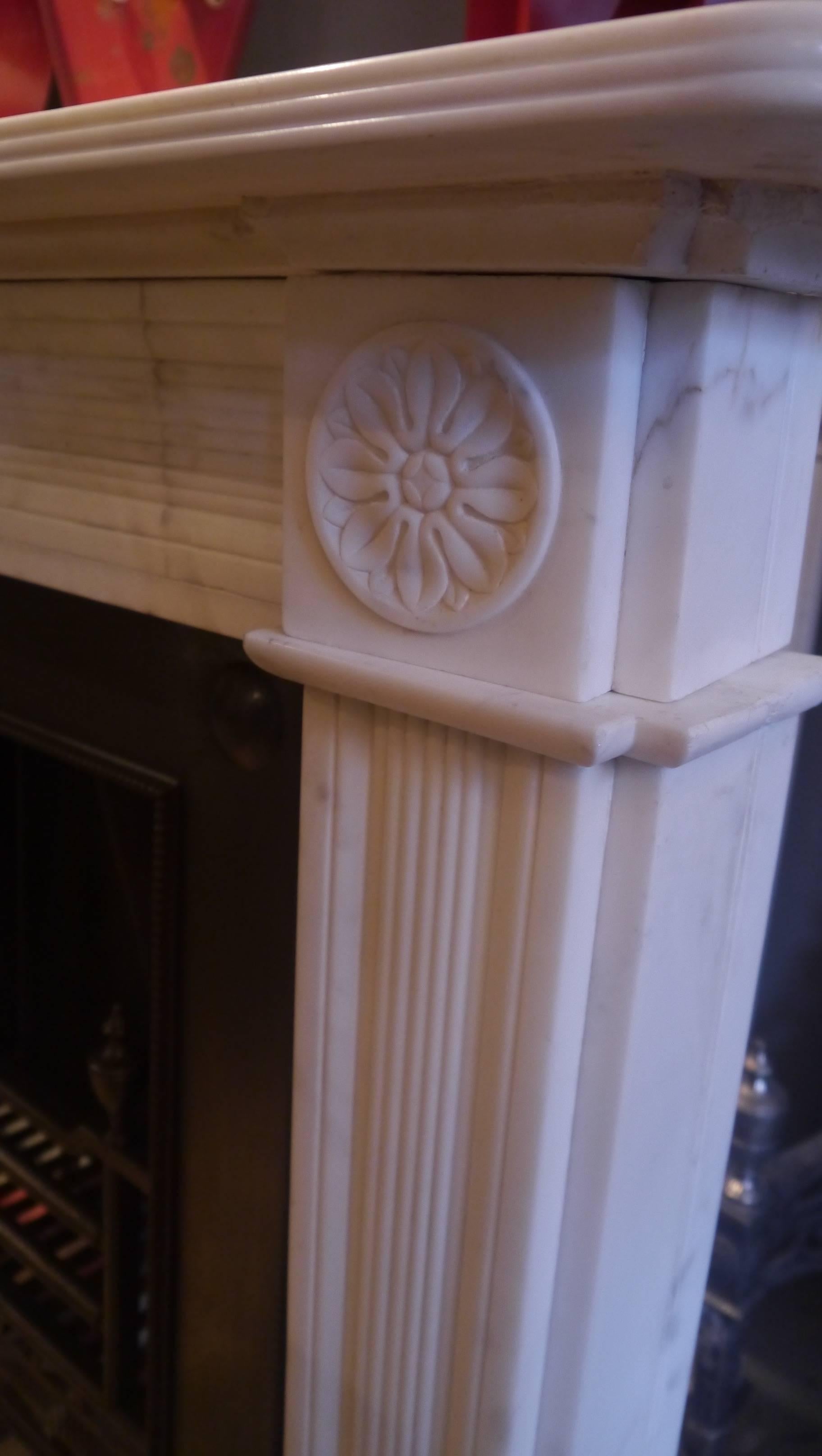 Original statuary white marble surround with floral cornerblocks, a centre plaque of an urn, reeded legs and frieze and with a double birdsbeak shelf, circa 1820. Opening 37.5