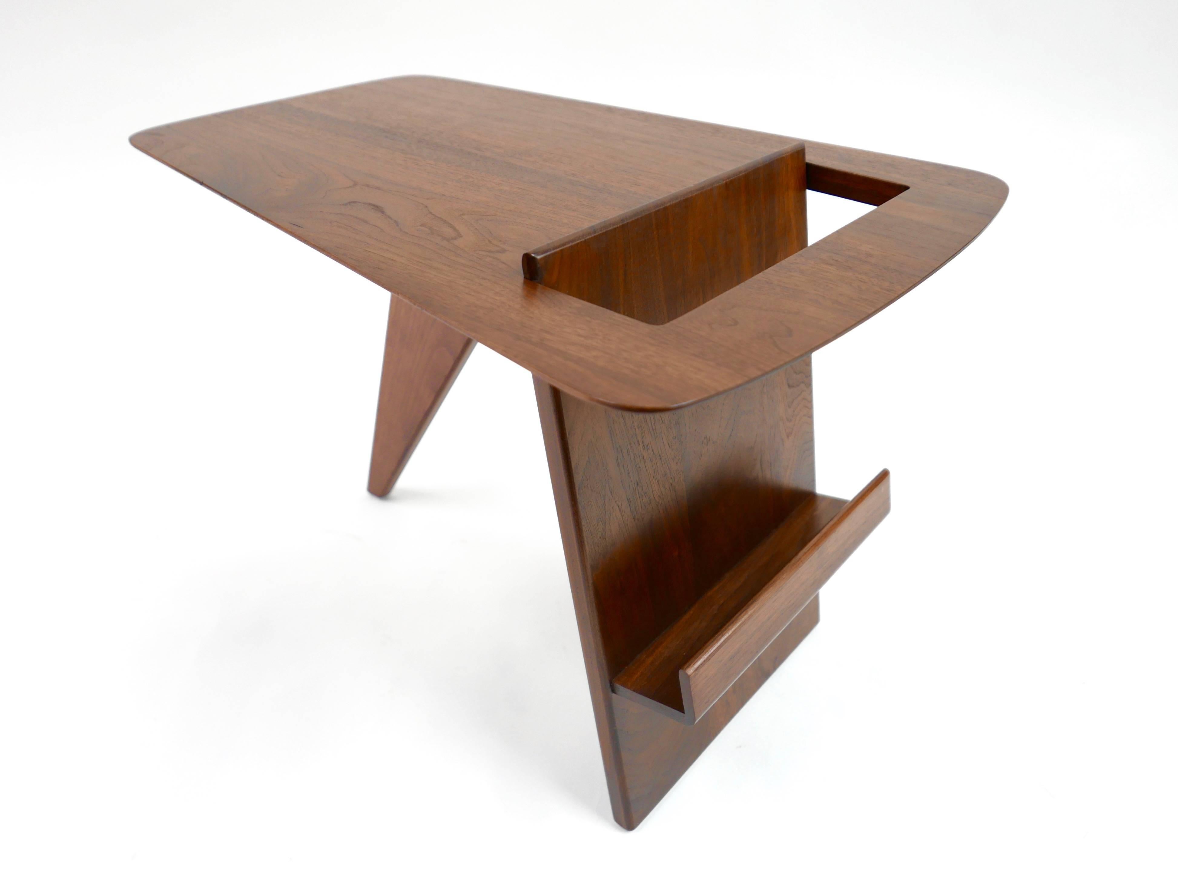 Walnut occasional table by Jens Risom. Offered by his company Jens Risom designs Inc. in 1949. This early design is considered one of the designers most dynamic. The leg serves as a book or magazine shelf.
This example has been beautifully