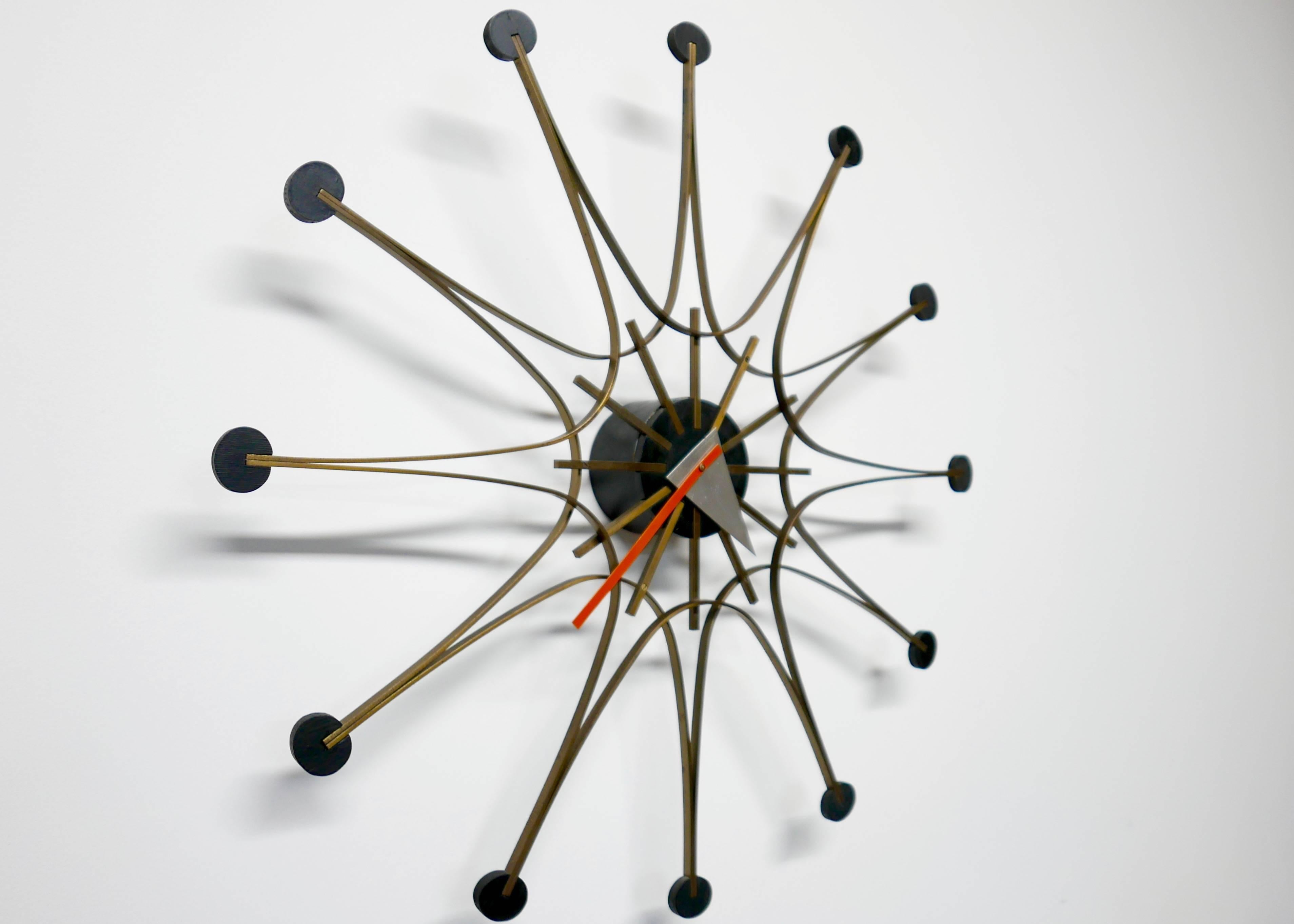 Howard Miller produced this rare George Nelson clock in 1957. The brass center is supported by aluminum rods and has lacquered wooden hour markers. This early form holds a mechanical key- wound driven movement.