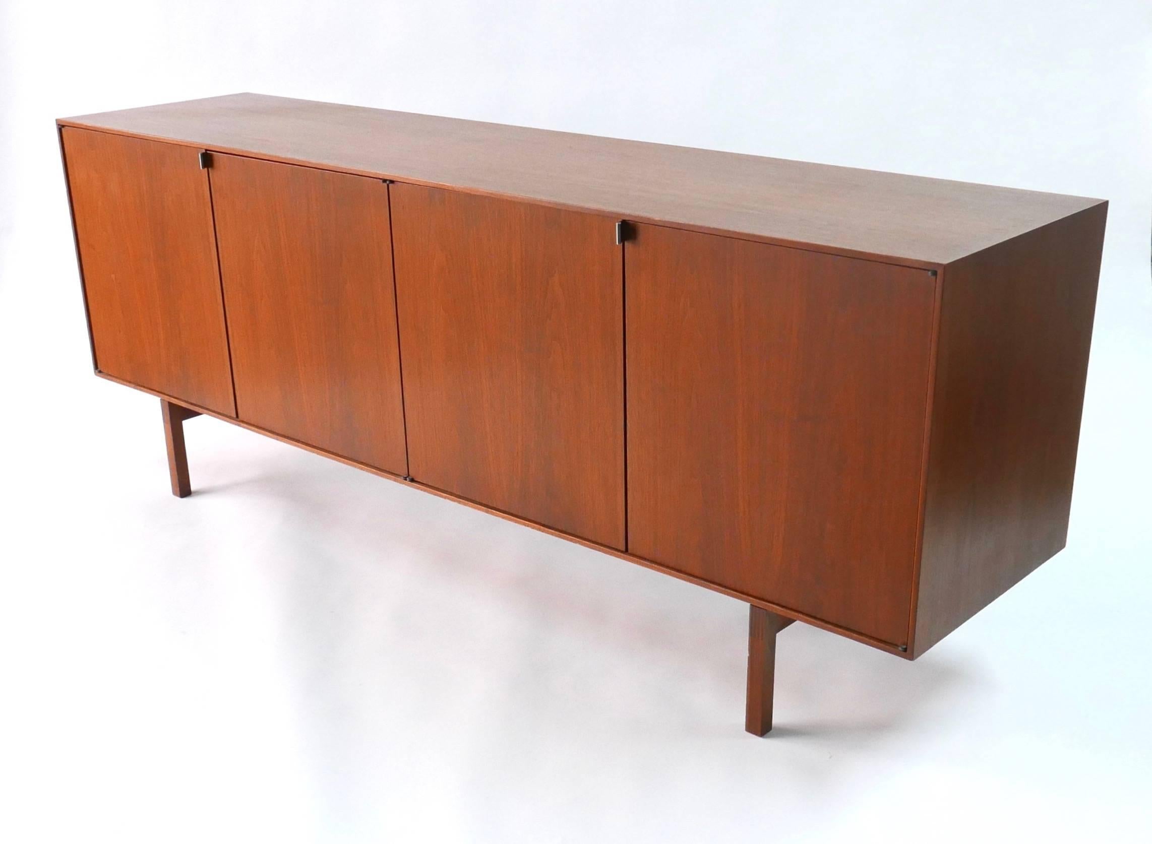 This walnut cabinet features four doors. The interior has adjustable shelves and two shallow divided drawers for storage. The underside of the cabinet is signed, Knoll Associates.
 