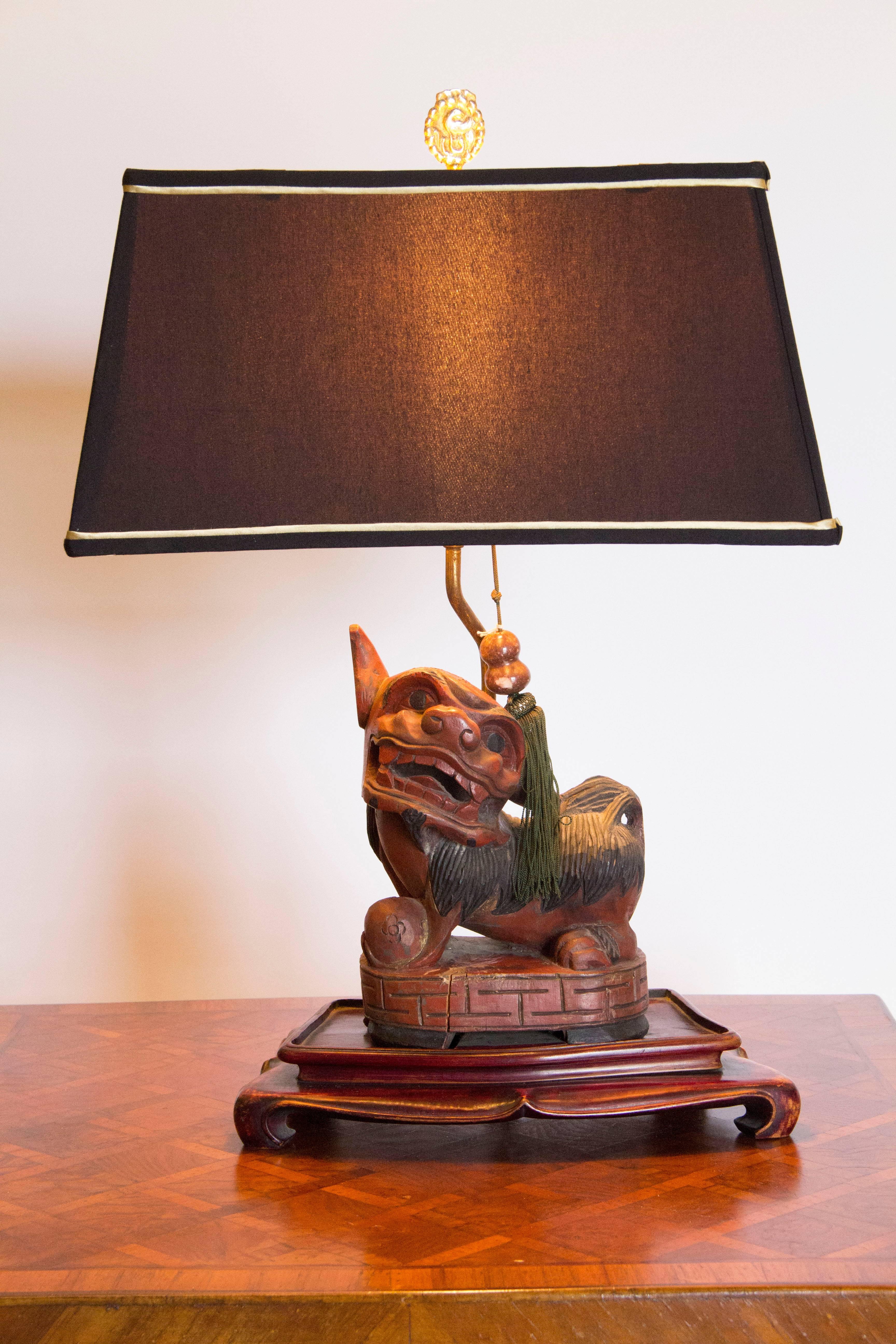 Whimsical foo dog lamp on an original wooden base recently re-wired and with a new Frederick Cooper black shade. The figure is mounted on a carved wooden base with original museum mount and an added jade tassel decoration that was original to the