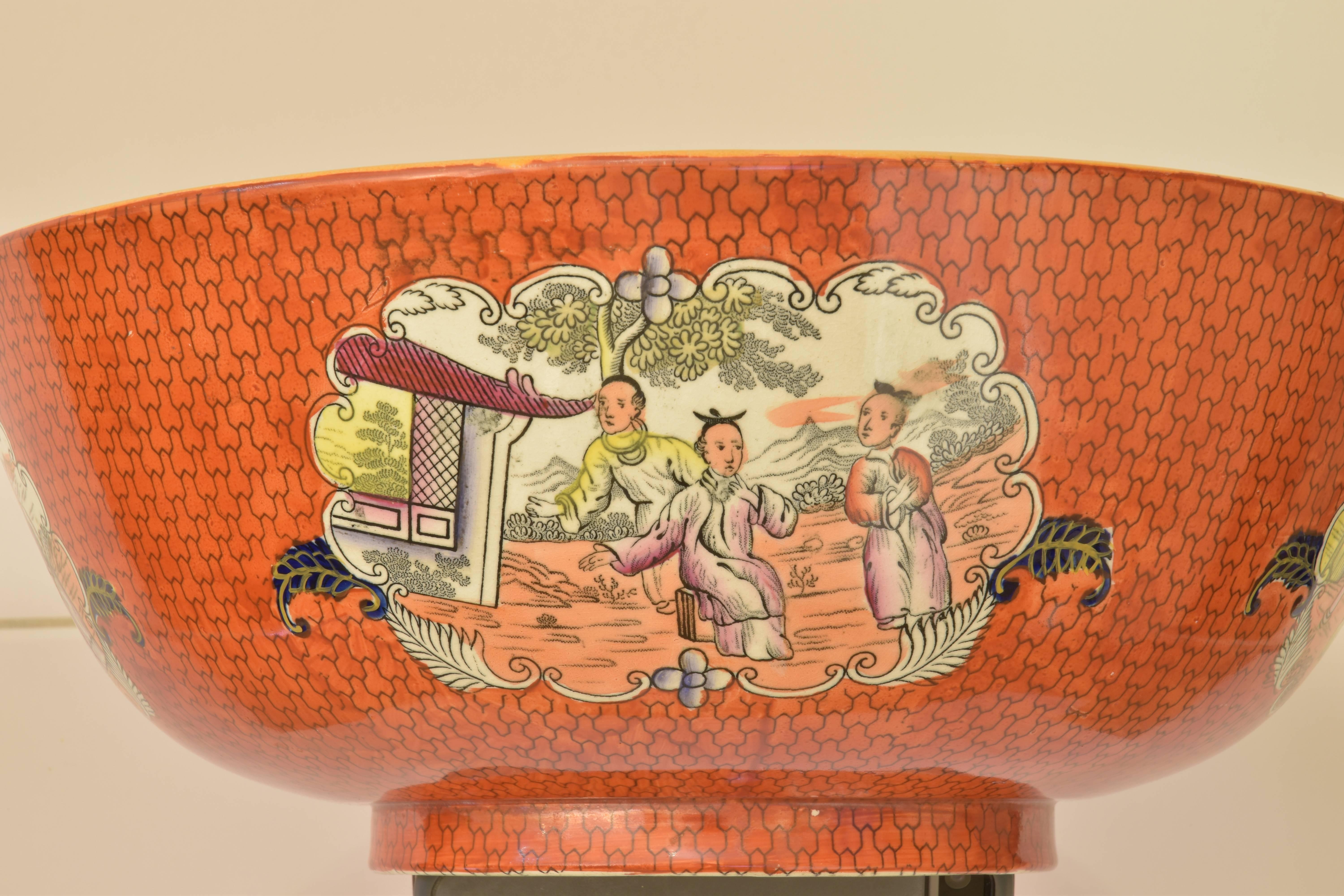 A Mason's Ironstone punch bowl in a striking salmon coloration with accents of green, yellow and deep blue with chinoiserie figural ornamentation on four sides of the bowl and in the centre of the interior of the bowl. A beautiful and highly
