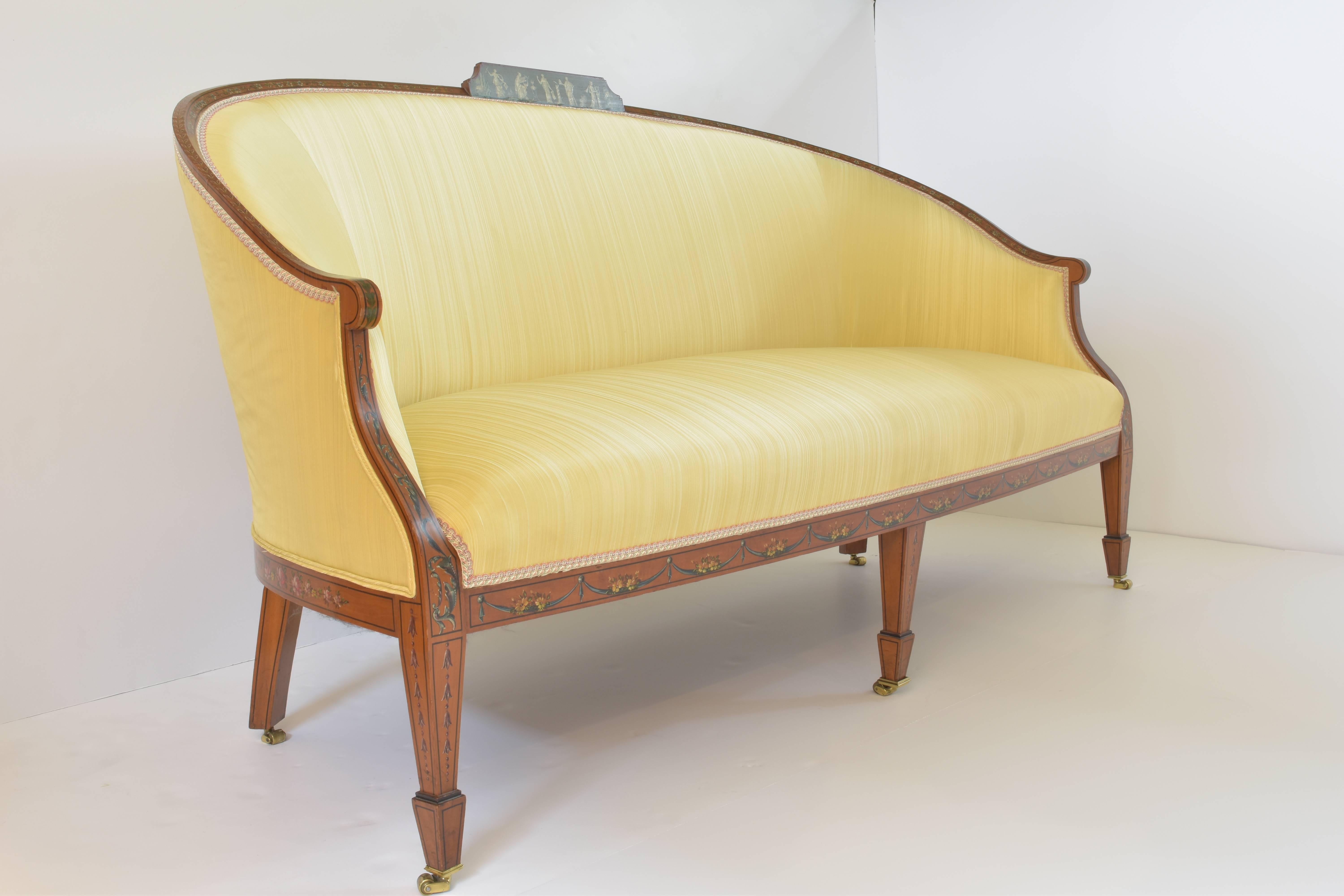 Antique English Sherato satinwood and floral painted sofa with an arched, rounded back sloping sides and arms with a bowed seat; upholstered in yellow silk, raised on square tapering legs, the back with neoclassical figures painted in a frame of