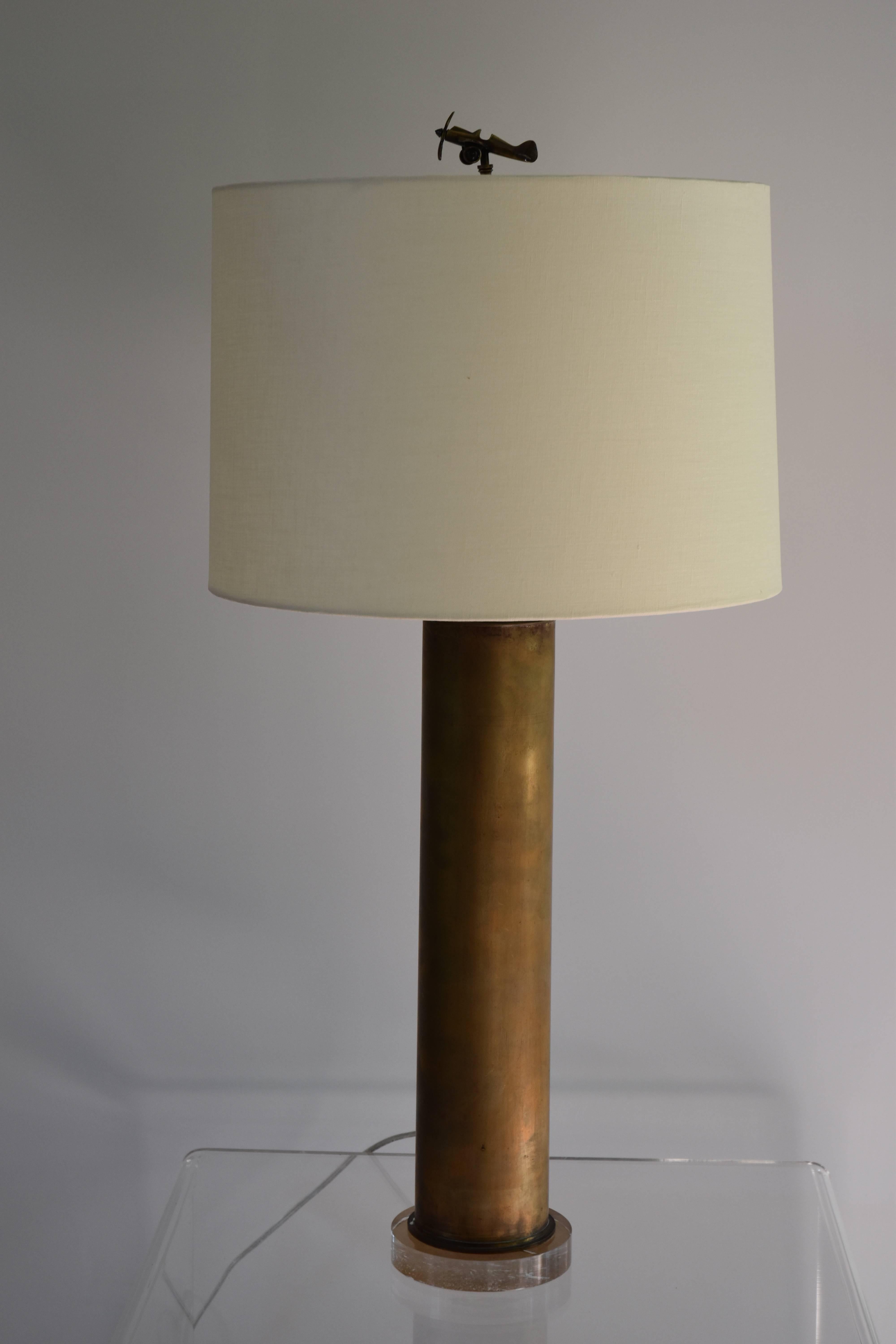 A vintage brass shell casing mounted as a lamp on a lucite base with a whimsical airplane finial. 