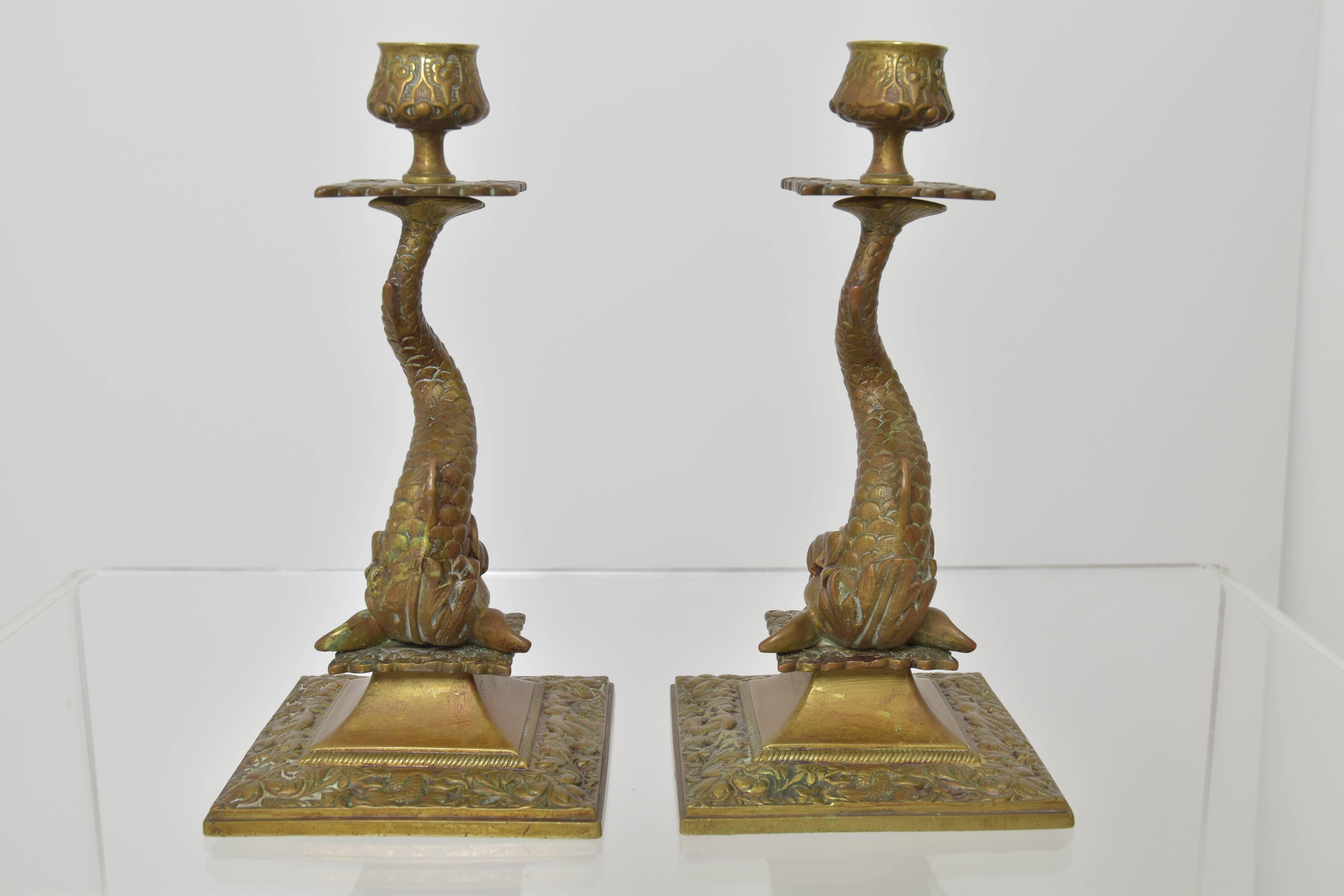 A charming and fantastic pair of cast bronze dolphin candlesticks with amazing floral, foliage and leaf details along the base. The large dolphins with upturned tails support the candleholders of each. These candlesticks are the perfect balance of