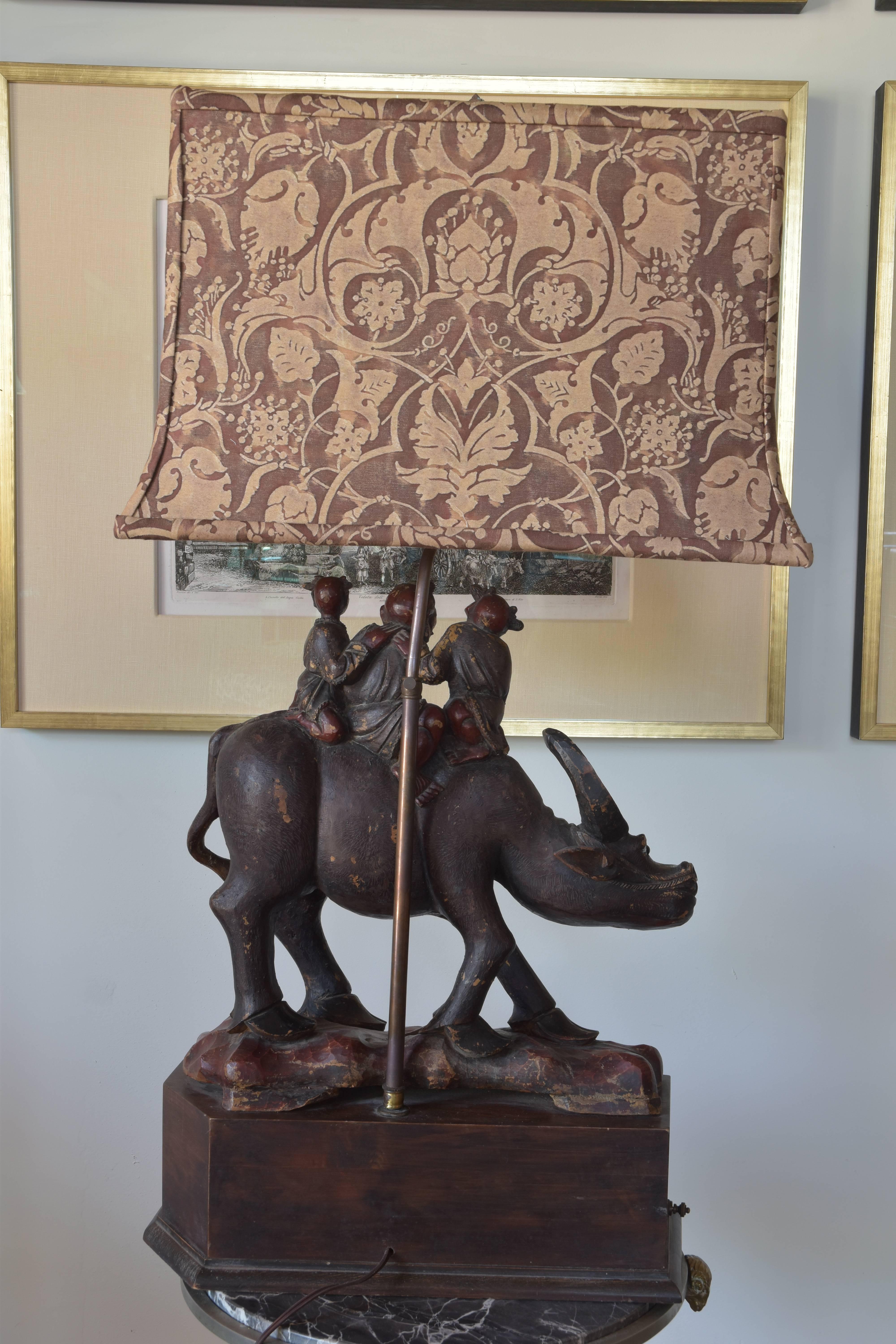 An exceptional Chinese export lamp from the early 20th century of an ox or water buffalo with three small children atop. The figure is 19th century wired as a lamp in the 20th century. A charming lamp with an amazing custom Fortuny lampshade