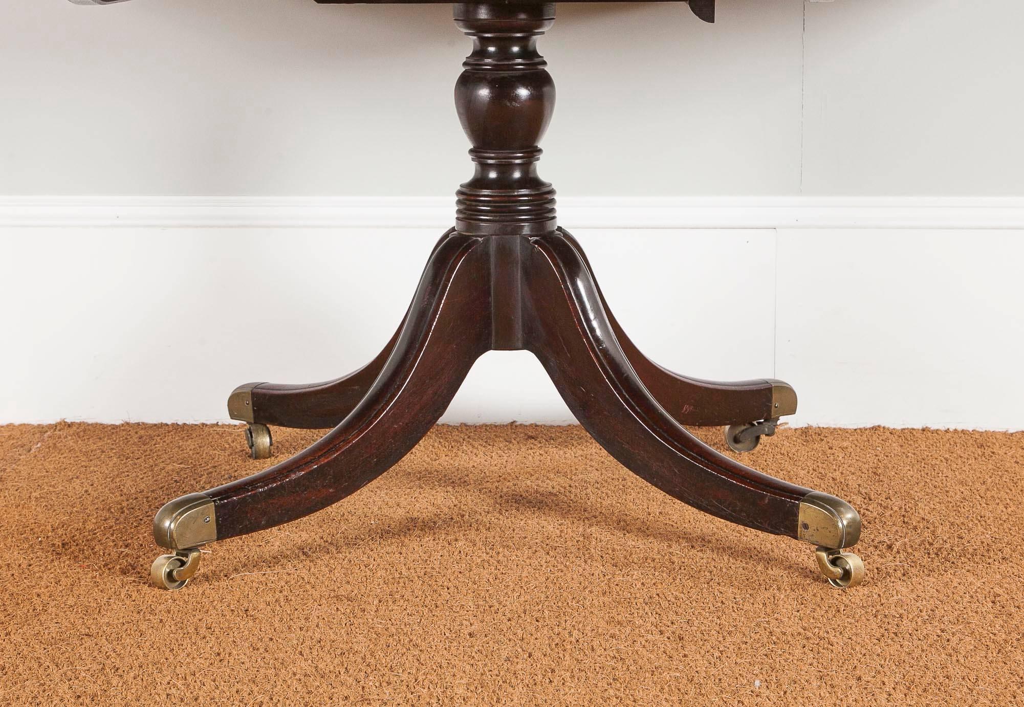 A fine large George III figured mahogany four pillar dining table, the rectangular top with a receded edge, resting on turned columns, each with receded four splay sabres, on brass toes and three later matched leaves, good medium brown color