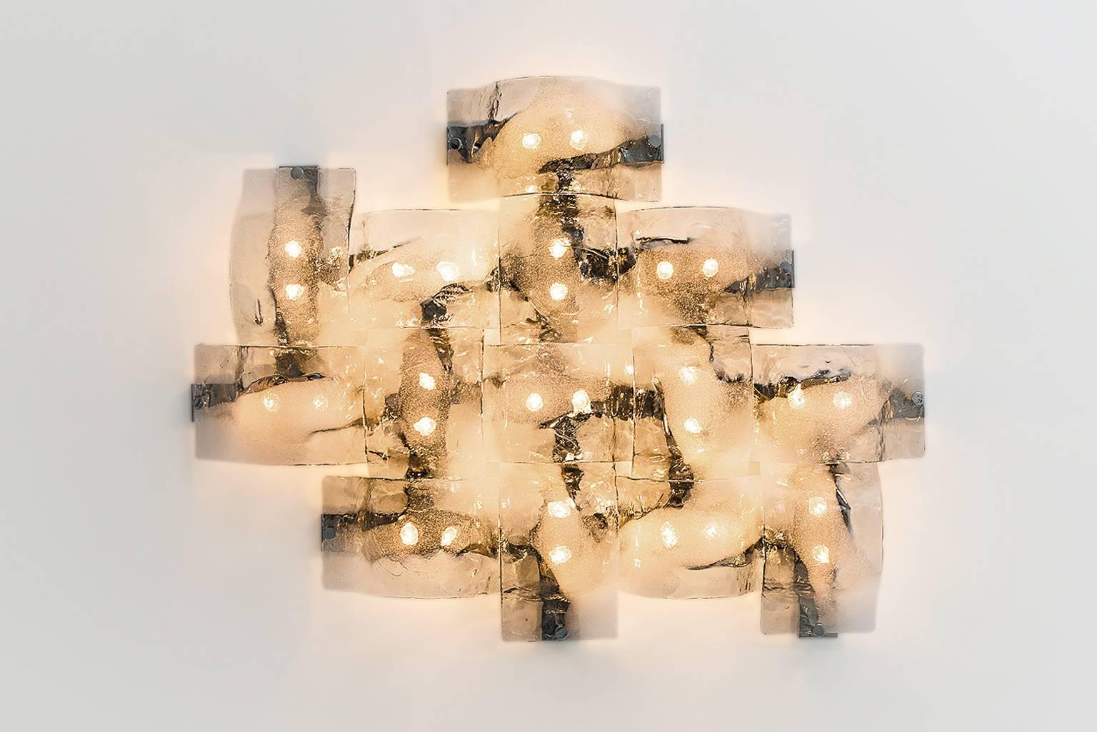 Impressive wall light sculpture by Carlo Nason for Mazzega, Italy 1960s. Composed of 14 handblown Murano glass sconces with each its own unique beautiful color gradient; from clear to light smoky with a cross line of white bubbled glass like the