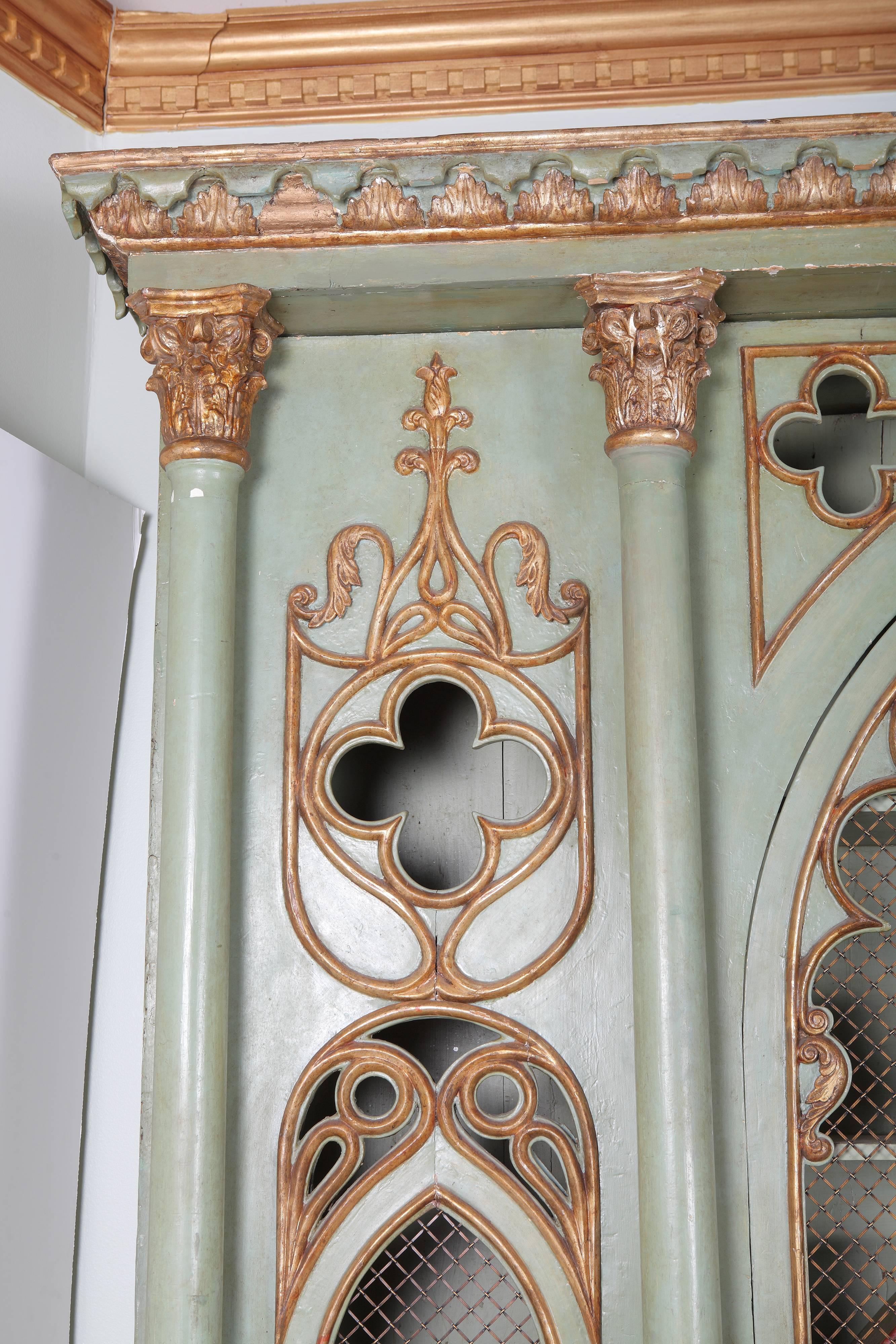 The cabinet exhibits a molded, out-swept leaf carved cornice above Gothic arch shaped grilled doors and trefoil carvings. The cabinet doors are divided and flanked by Corinthian column pilasters which rest on a paneled base with breakfront outline