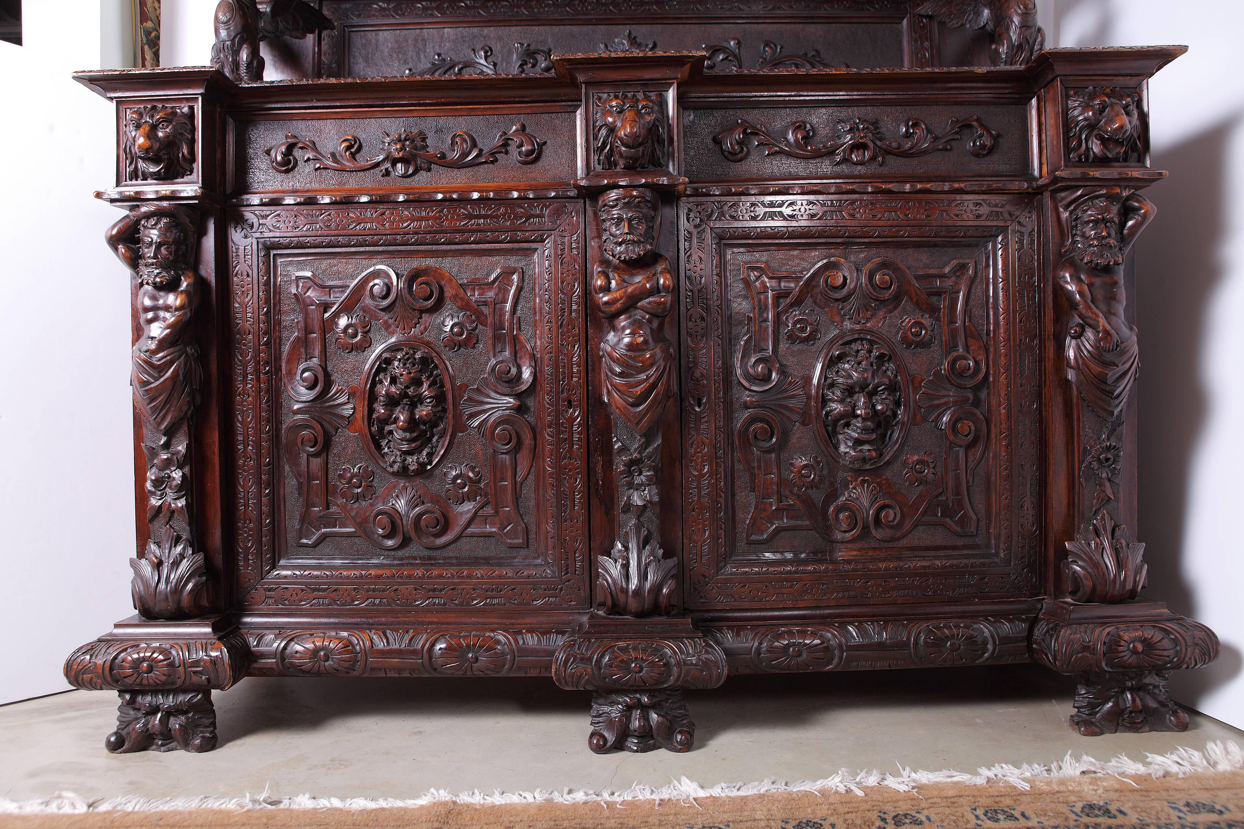 Heavily carved Italian Renaissance Revival sideboard featuring sculptural depictions of winged griffins, lions heads and figural atlas supports. In addition to the upper shelves and the lower enclosed cupboard, there are two hidden drawers. Key to