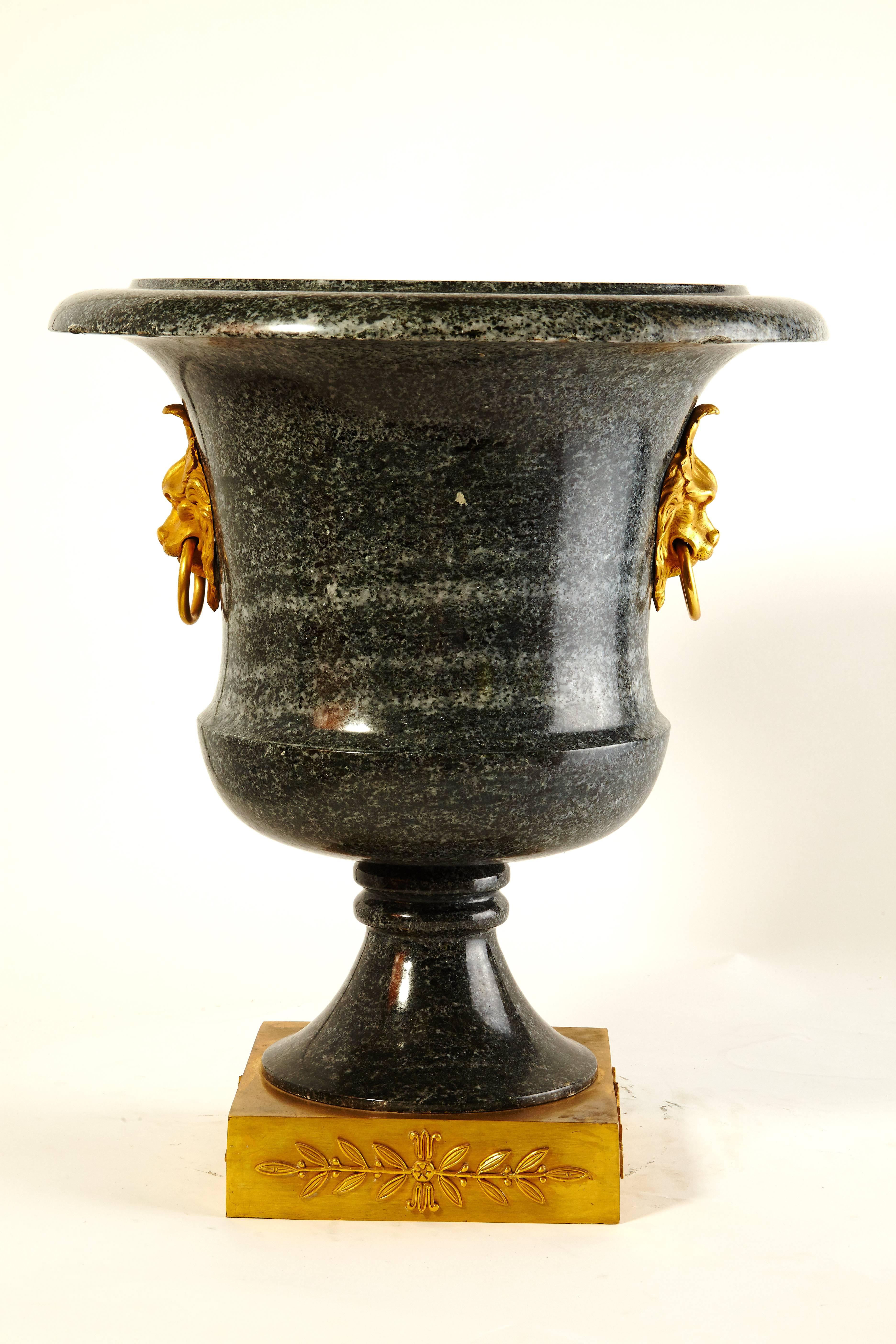 Pair of exceptional neoclassical campagna shaped green granite urns mounted with finely chased gilt bronze lions' heads and sitting on finely executed gilt bronze bases decorated in relief with a classical motif of laurel leaves and berries.