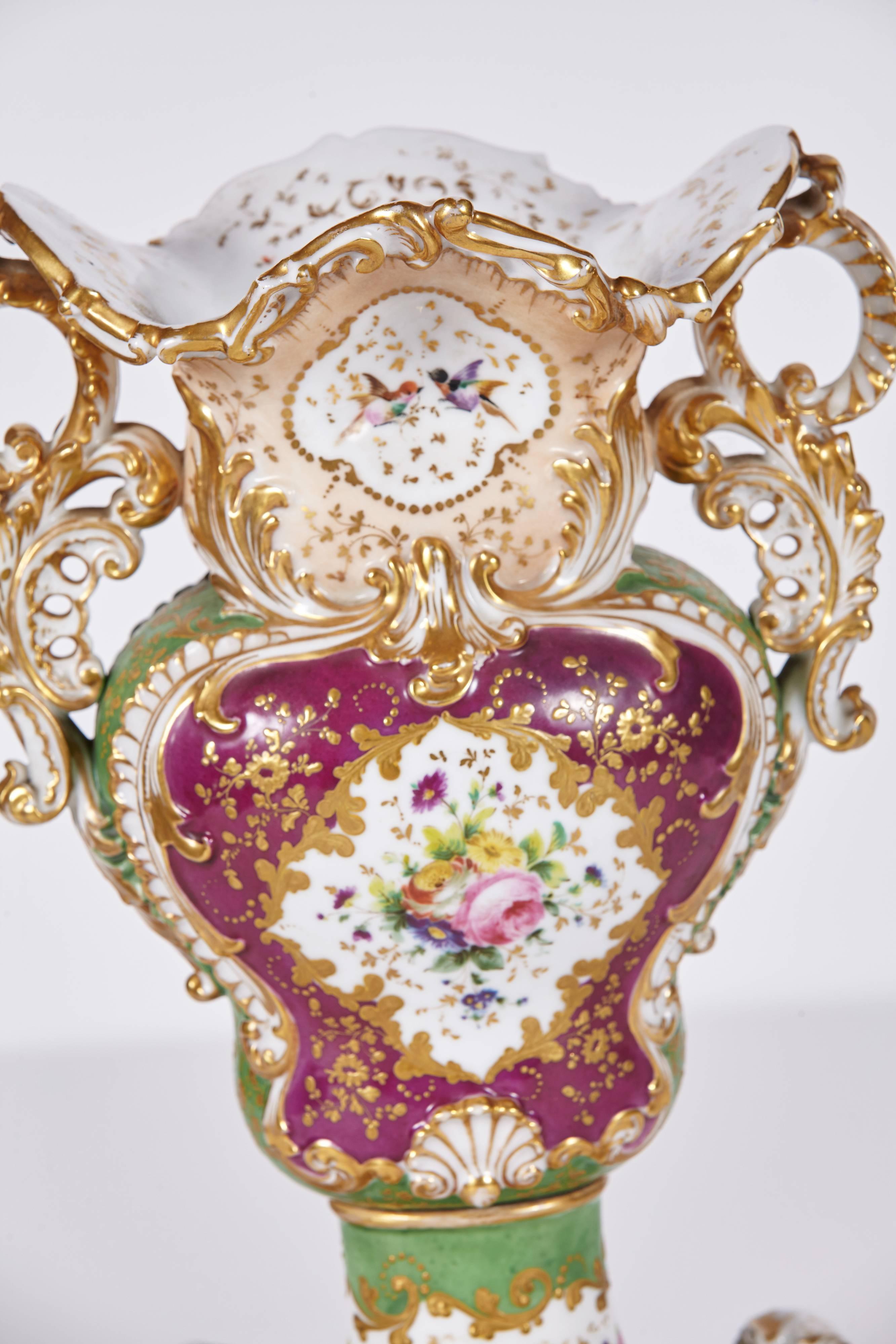 Beautiful pair of Old Paris porcelain vases signed by Jacob Petit. Rococo style vases in tones of purple, green, and dusty pink mounted with original threaded brass bolts onto matching plinths. Reserves hand-painted with birds and flowers and