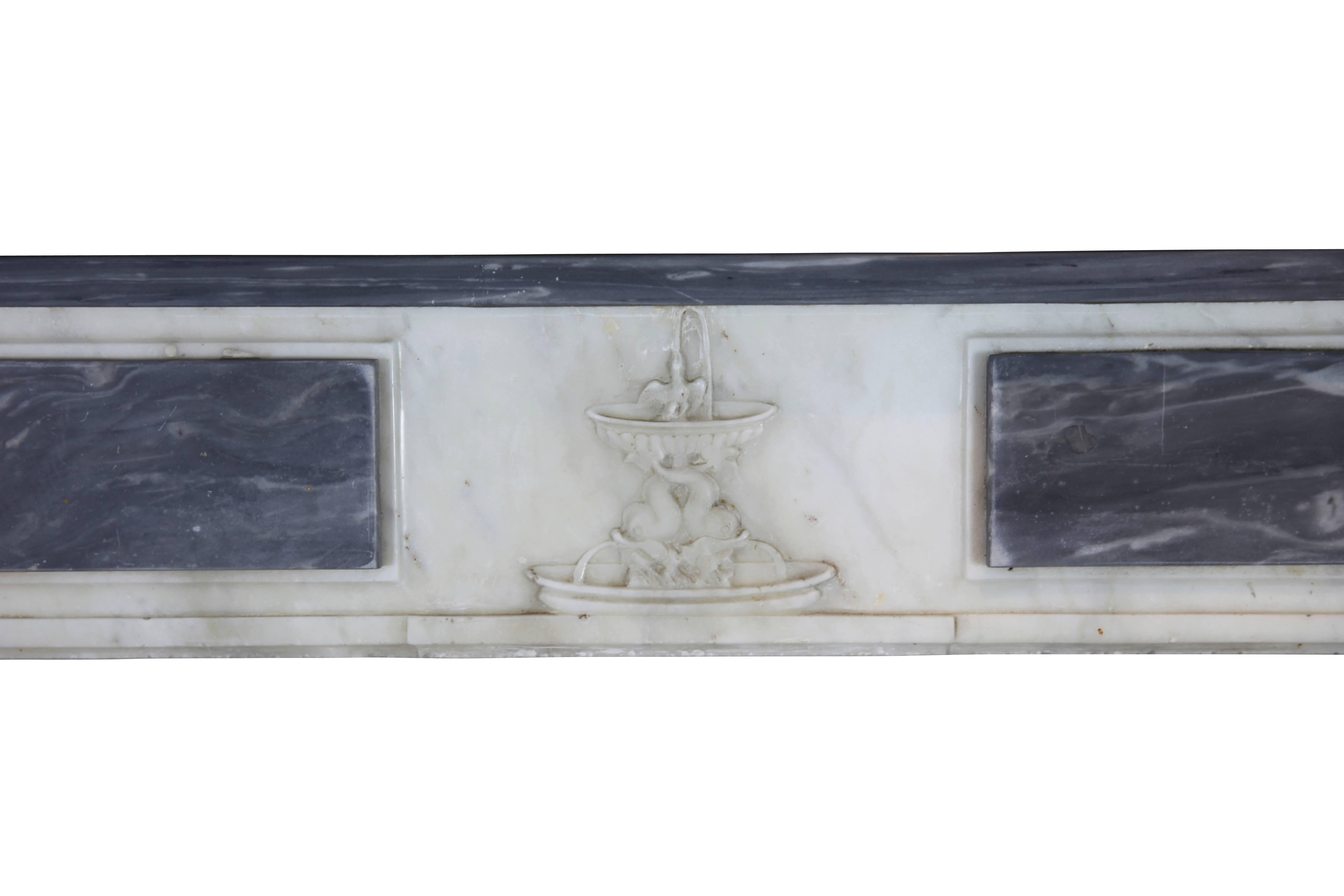 The fine original antique fireplace mantel is one of his kinds.
The combination of the Bleu Turquin marble with Blanc de Carrara marble is perfect.
The fine carving of the center piece which brings a fountain and the medallion on the extremes of