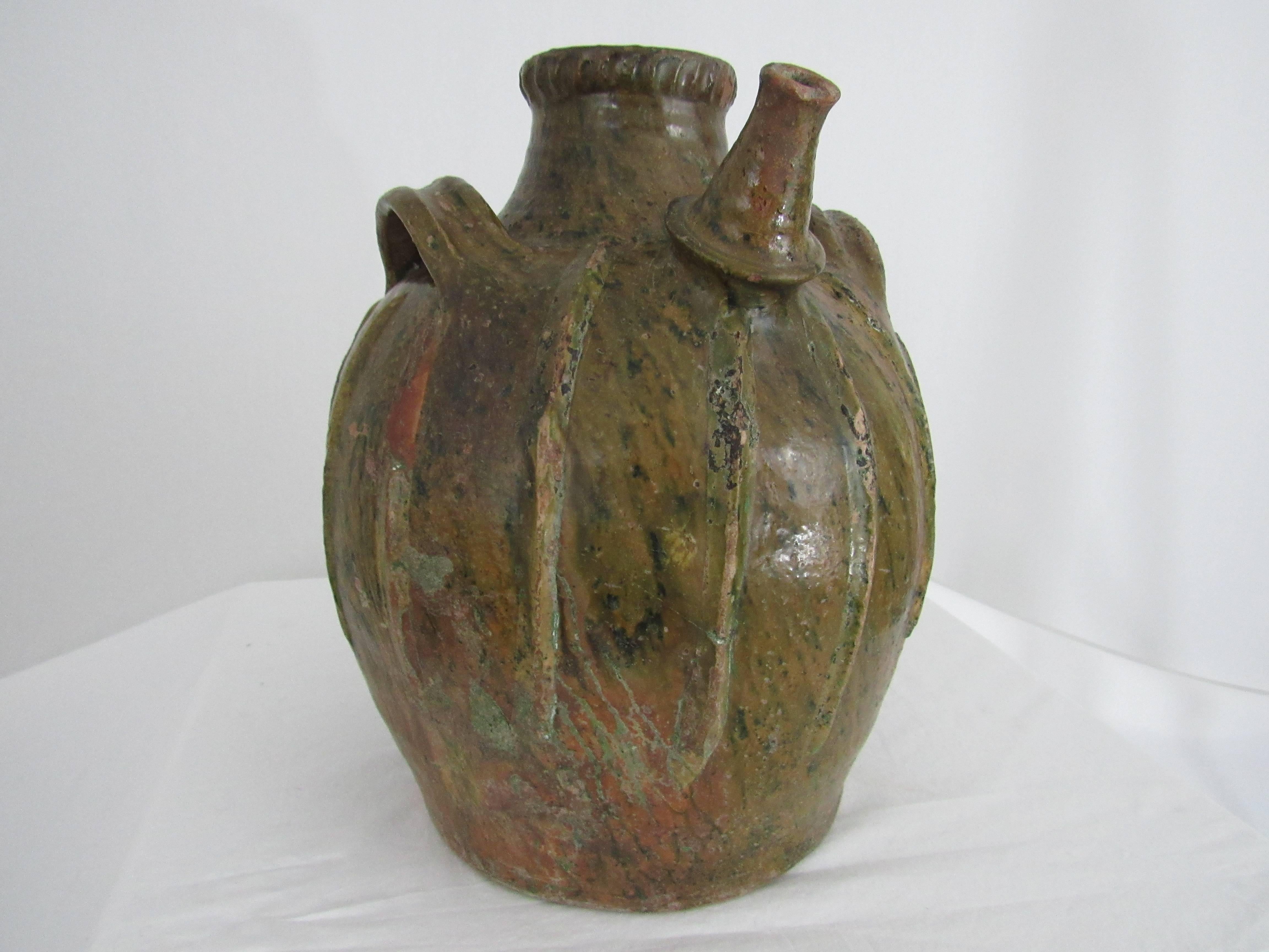 French oil jar from Auvergne region in France. A three-handled green-glazed terracotta storage vessel, with pouring spout. It has a wonderful textured surface, in part due to the scaled and ribbed decoration applied onto the body. There is variation