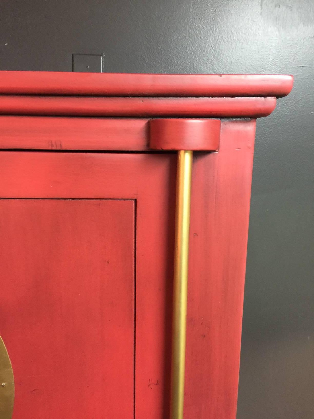 This vintage cabinet is made of solid hardwood with brass hardware which has been painted gold. It has been professionally lacquered in red with a dark glaze. Perfect storage for china or service ware or can hold a tv in a den or bedroom. A great