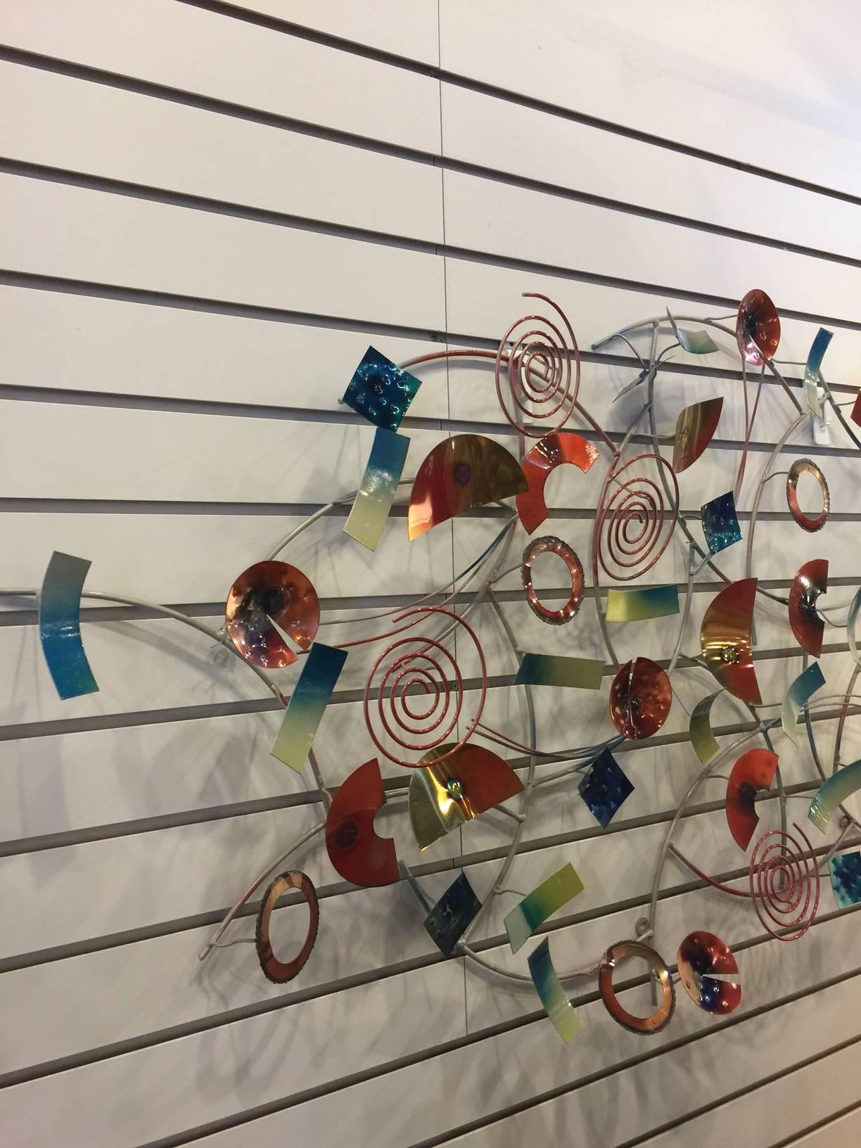 This colorful enameled metal wall sculpture is created in the style of Curtis Jere. Designed in California, manufactured in China. This piece is comprised of an array or painted metal shapes and configurations welded to a background of circles of