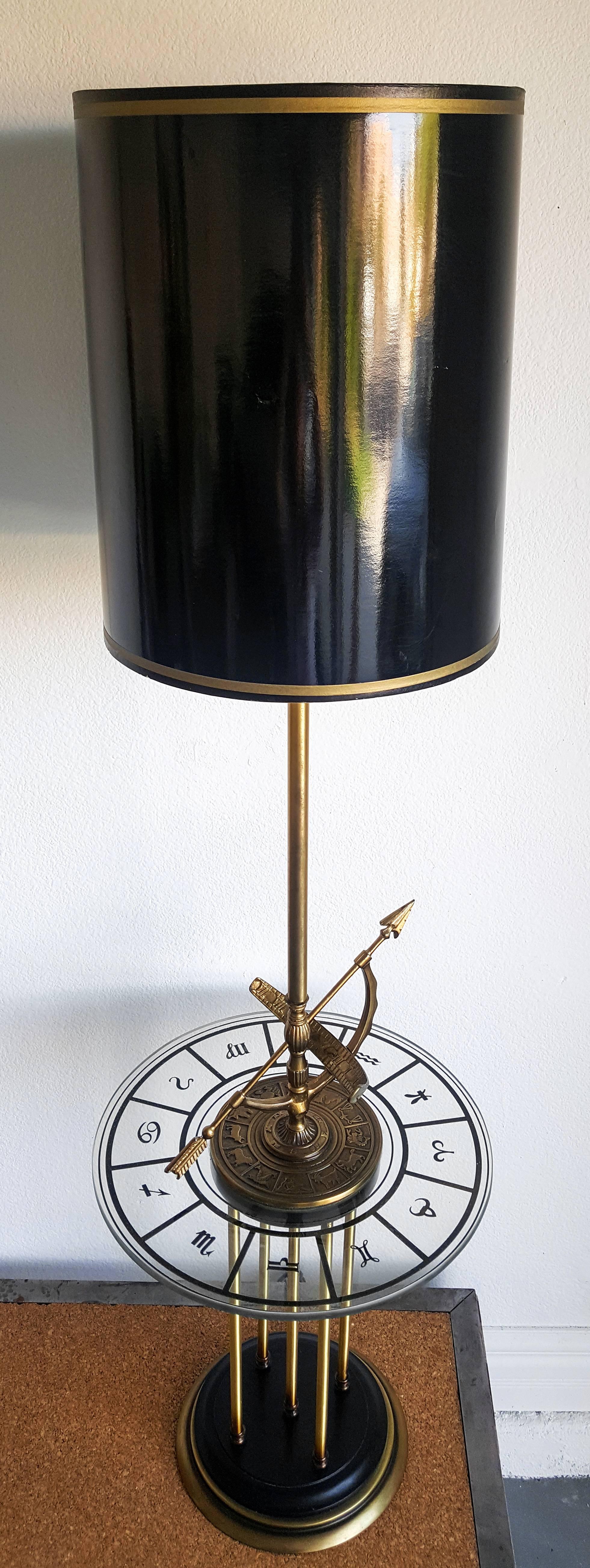 A stunning piece of Mid-Century design, this 1960s floor lamp features brass and bronze construction with a thick glass table mounted in the middle.

The glass table has each astrological sign in gold leaf. The brass plate that rests the middle of