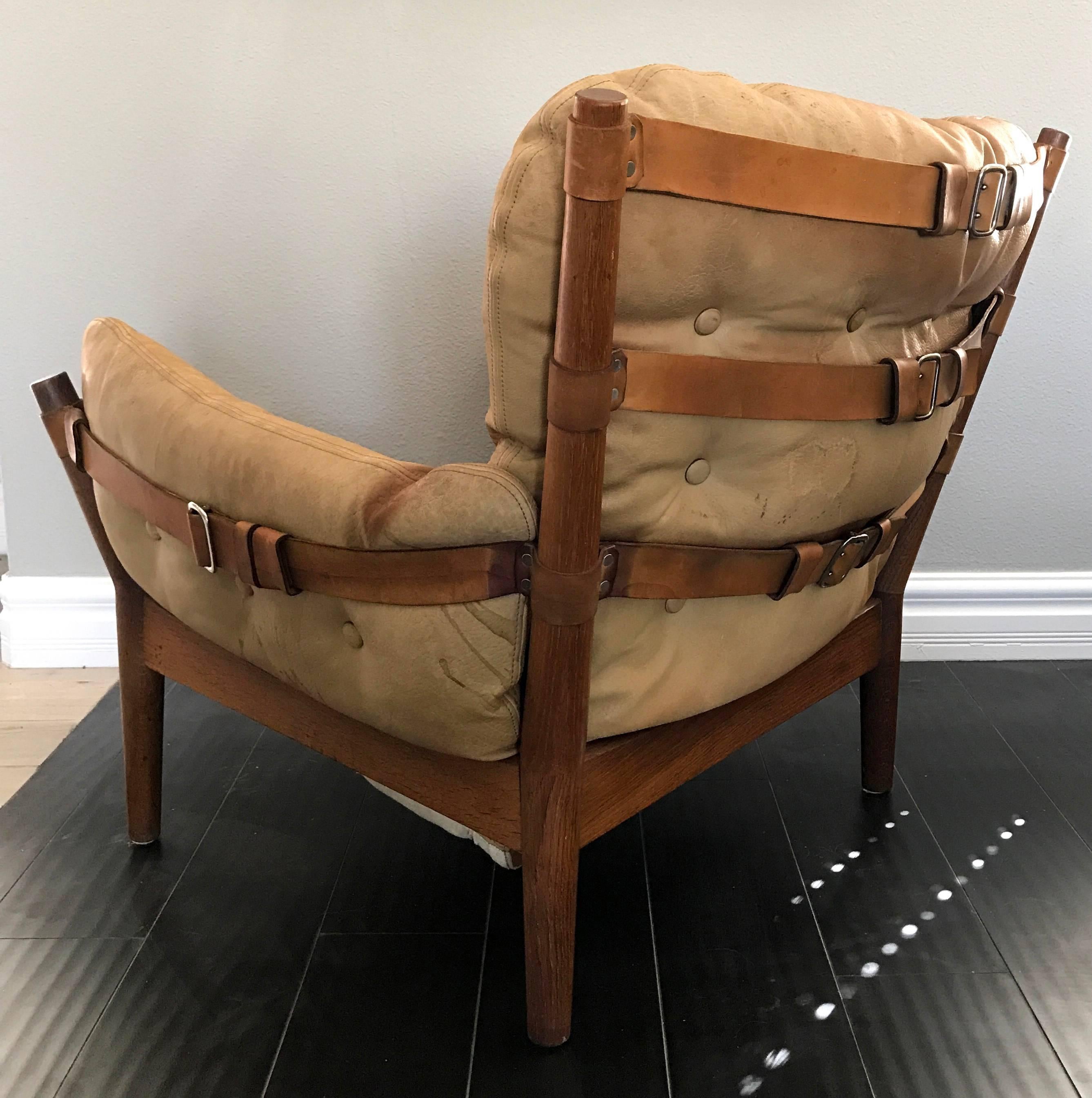 A rare low-slung easy chair by John Mortensen for Magnus Olesen (Denmark). This stunning lounge chair appears almost as a more masculine version of a Norell safari chair, featuring a triple leather-belted back, as well as belted arms and stunning