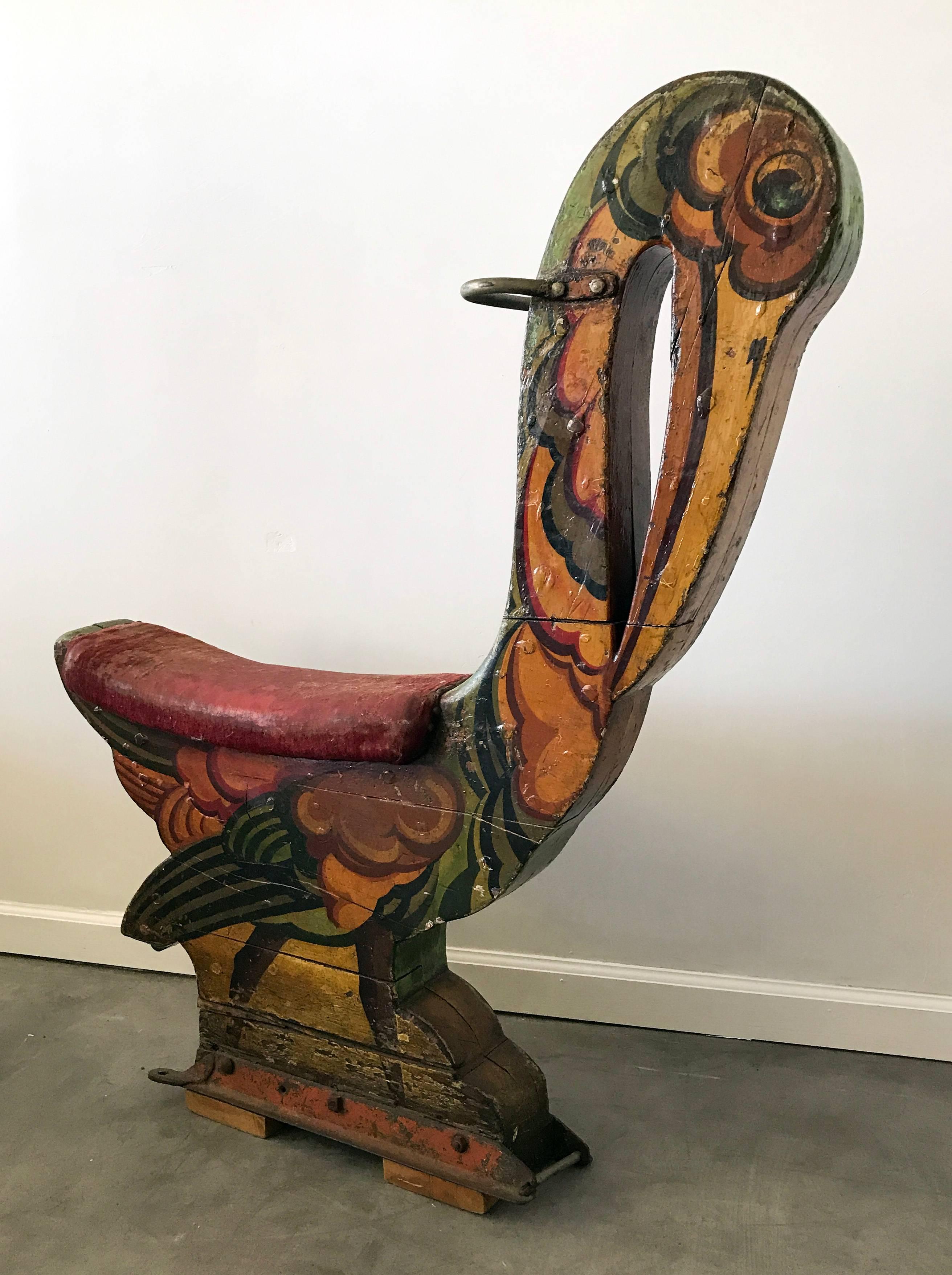 Gorgeous colorful piece of Folk Art. This 1920s English carnival bird ride has layers and layers of paint from years of use; age splits on the wood, and a well worn wooden saddle with worn and threadbare red velvet upholstery with nailhead trim.