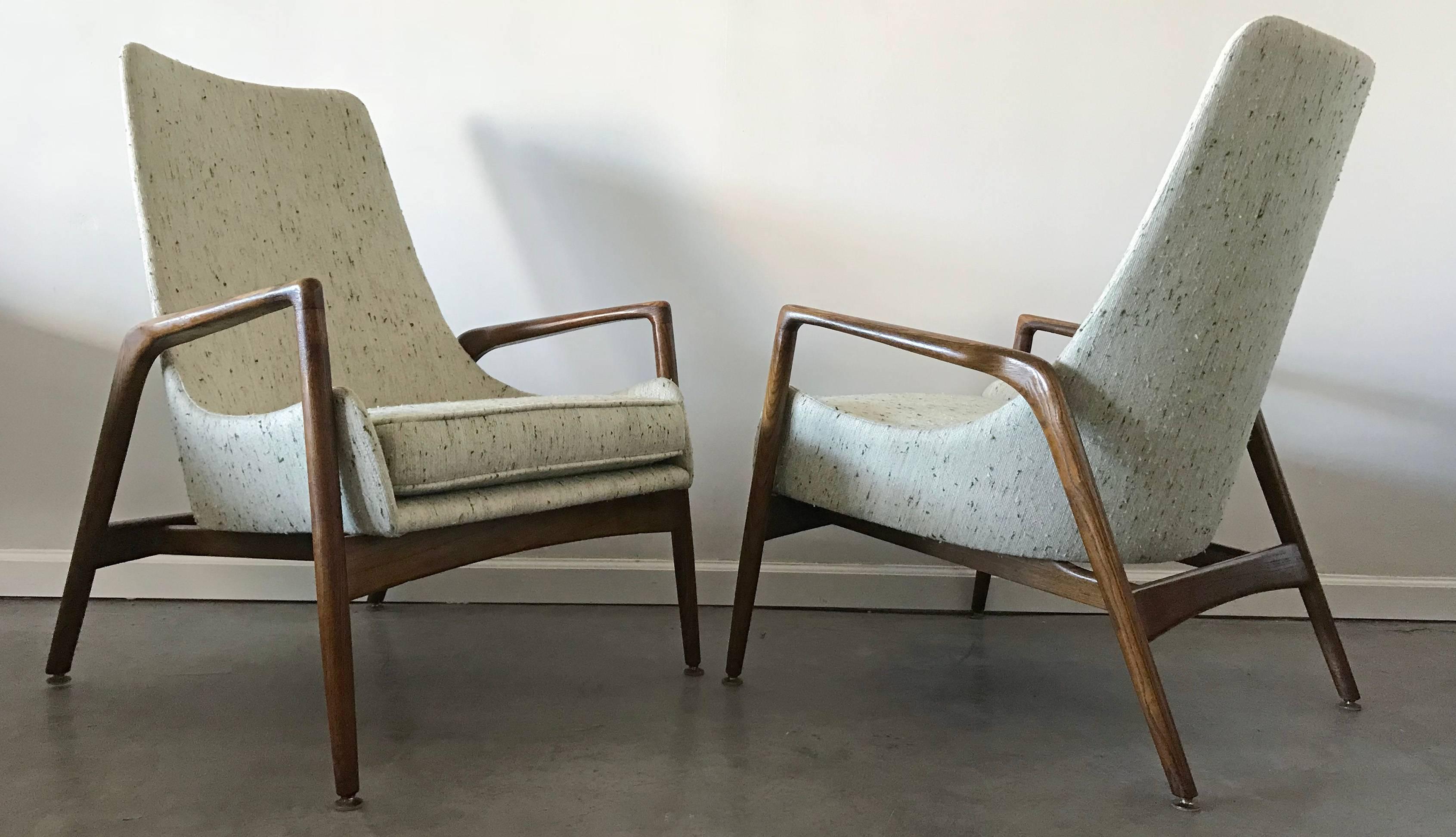 A rare, early pair of Ib Kofod Larsen high back lounge chairs. These early lounge chairs feature clean modern lines and timeless design on their original, unrestored walnut frames, with incredible patina. The chairs have been reupholstered in a