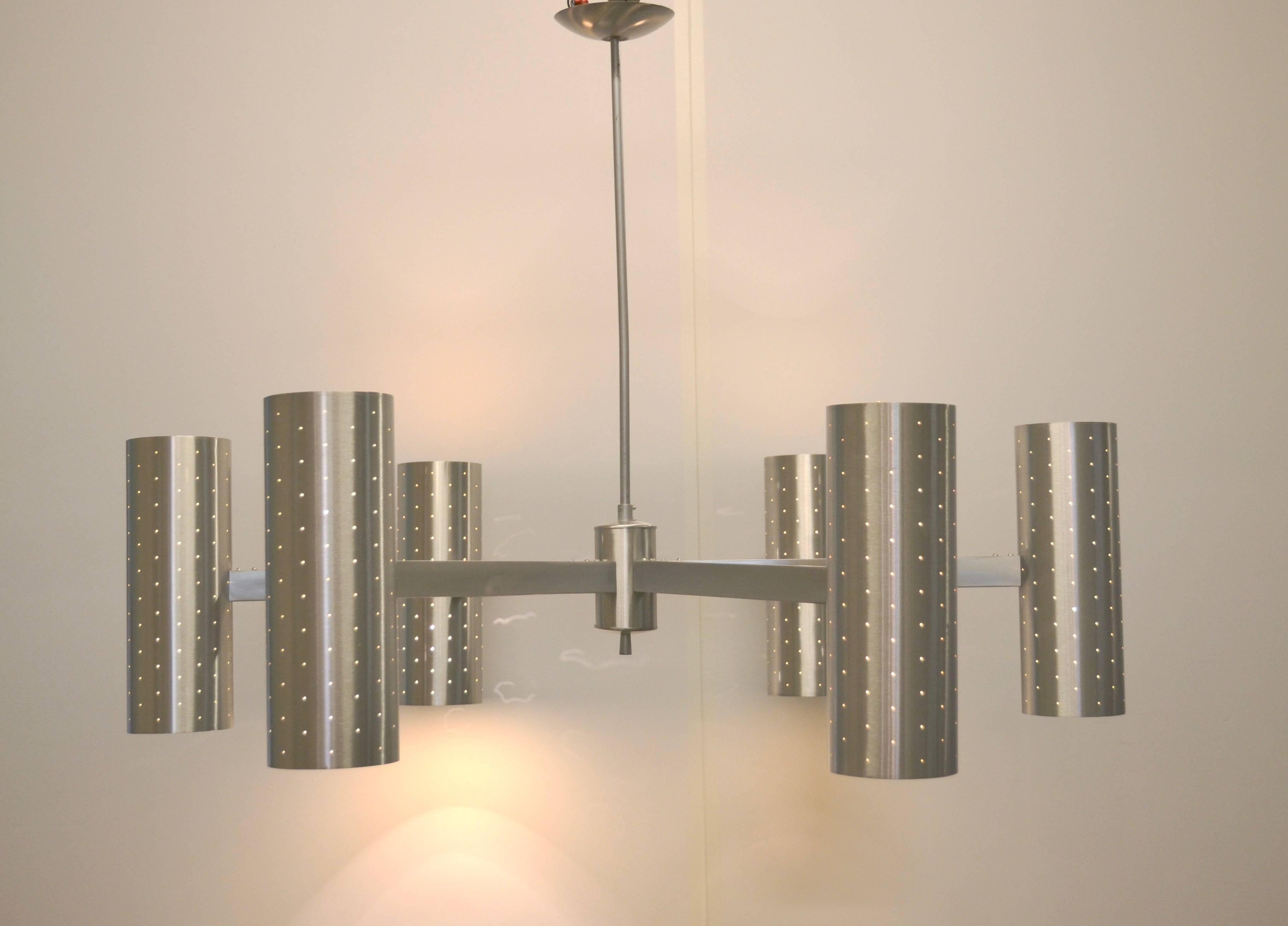 Monumental mid-century modern six armed pendants. Brushed aluminum cylinders emit light from top and bottom (two bulbs per cylinder) and have perforations.  Large scale at 4' diameter. Pair available, but sold individually. With hanging rod