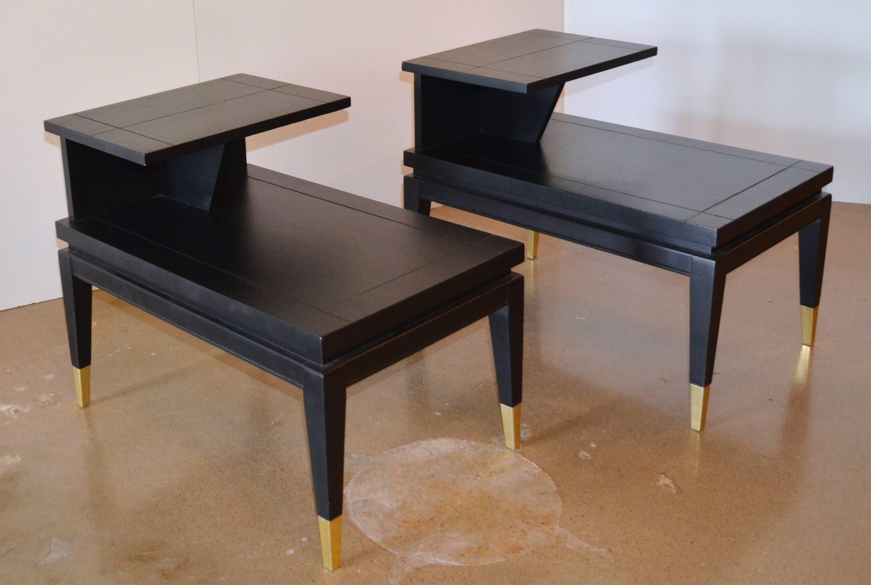 A Mid-Century Modern pair of two-tiered end or side tables in a black ebony finish with brass capped feet. Could also be used as nightstands. Manufactured by the Lane Furniture Company. Marked on bottom - Lane Style no 1687 Serial no 752030.