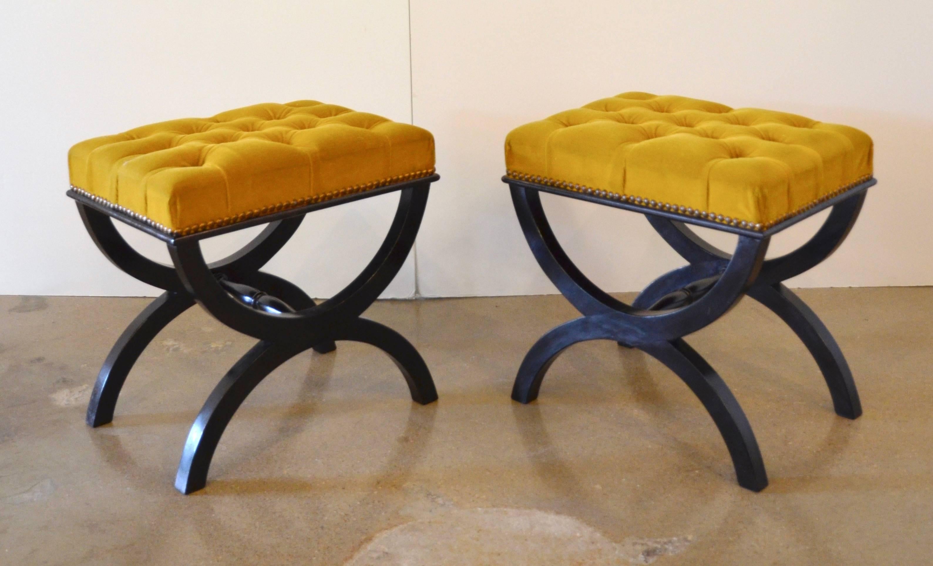 A pair of black lacquered hardwood benches or stools in the curule form with gold velvet button tufted upholstery and brass nailheads, circa 1950.
