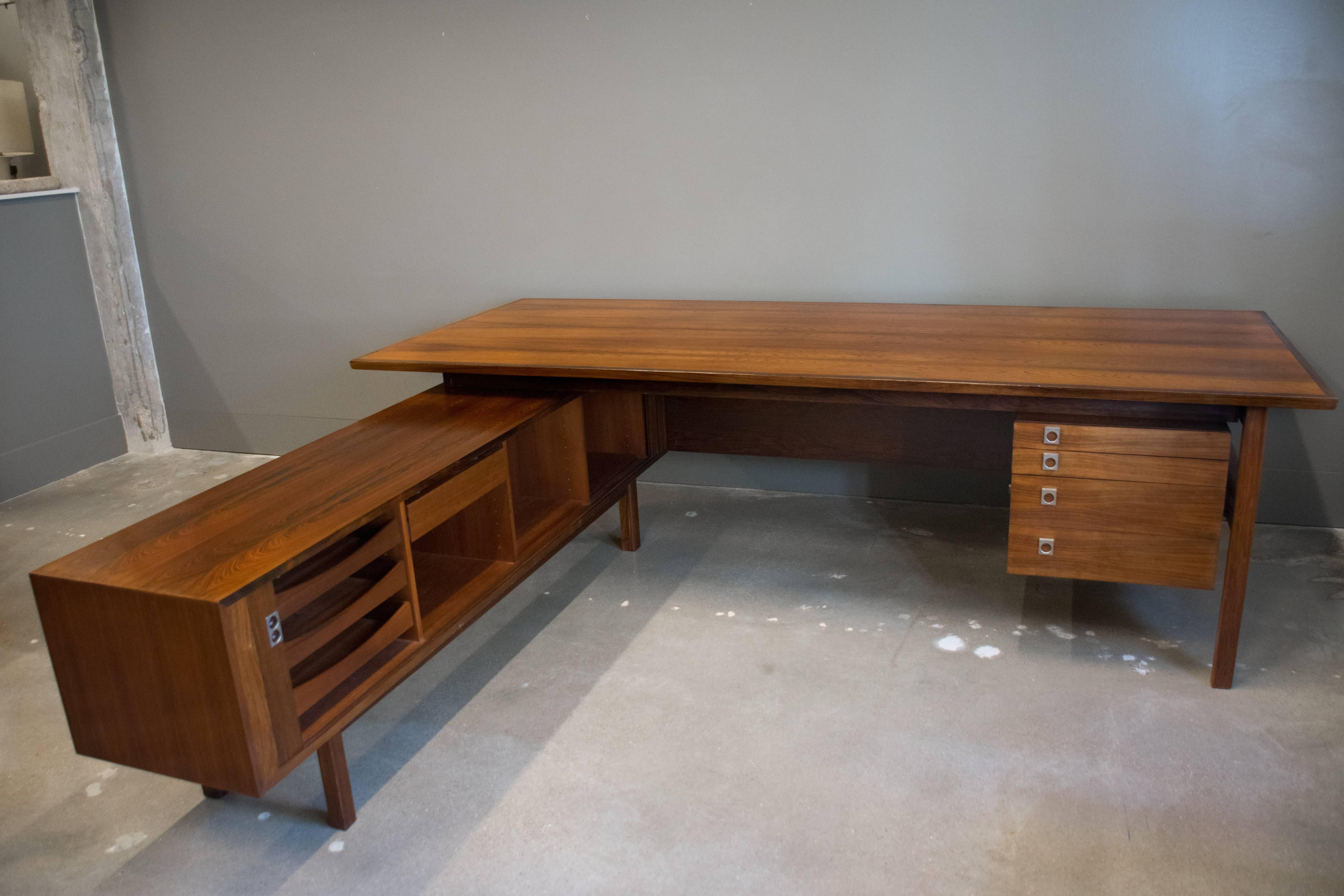 Danish MCM rosewood L-shaped executive desk, circa 1960, designed by Arne Vodder (Denmark, 1926-2009) for Sibast Furniture. L-shaped configuration. Primary desk with kneehole and stack of four drawers, credenza extension with dual tambour doors