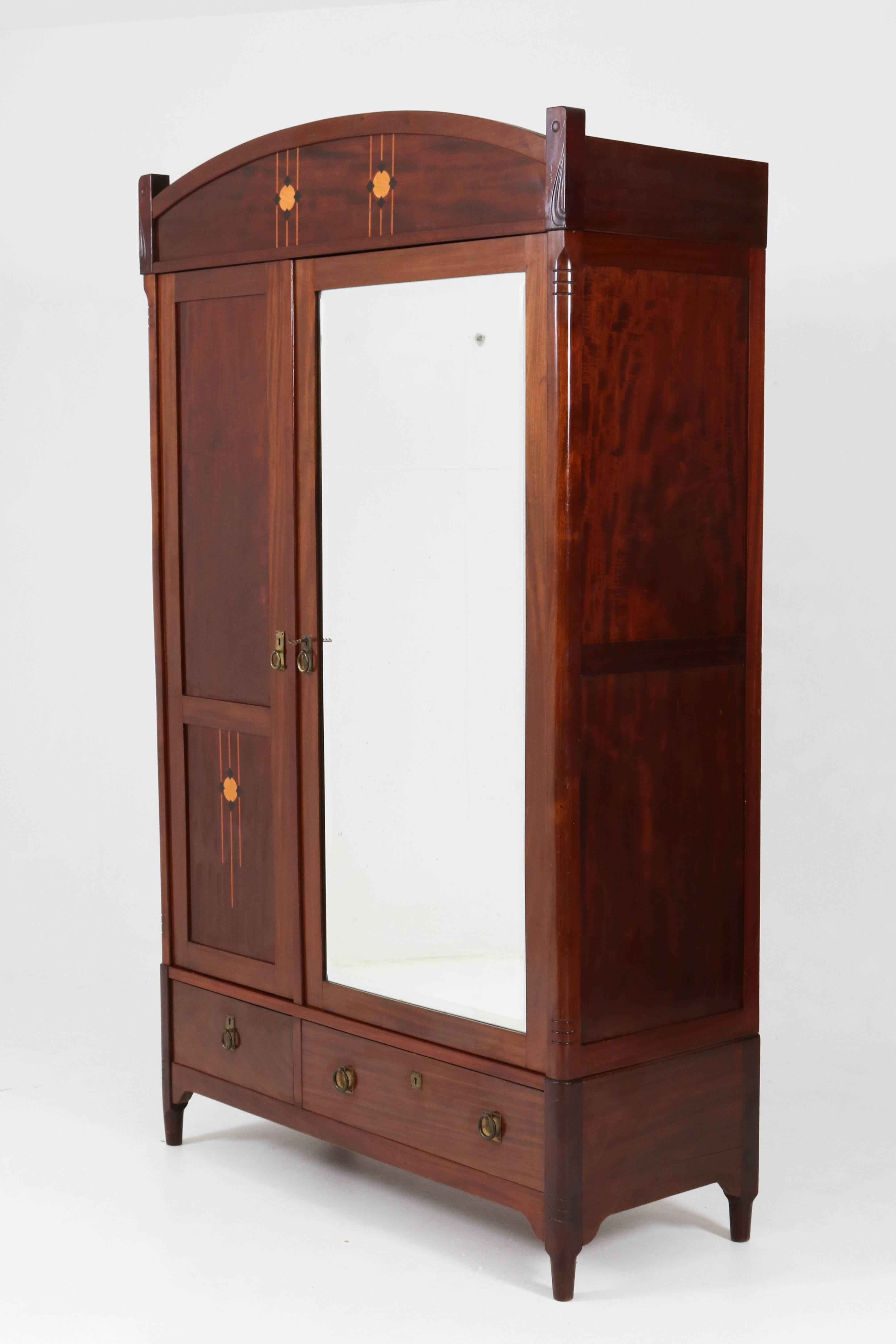 Stunning Dutch Art Nouveau wardrobe or armoir by H.Pander, 1900s.
Solid mahogany with stylish inlay on top and left door.
Solid brass handles on doors and drawers.
Original beveled glass mirror.
Three adjustable wooden shelves.
In good original
