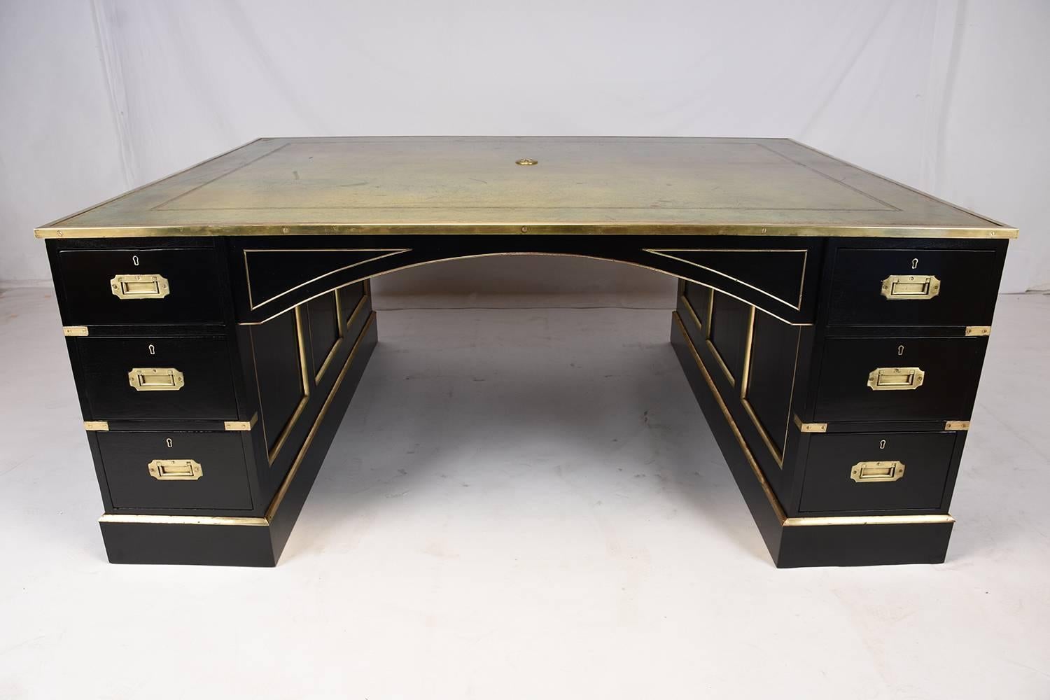 This 1900 Antique English Campaign-style partner desk is made of wood with a beautiful ebonized finish. The top of the desk features the original embossed leather work area with beautiful gilt trim details. There are twelve drawers throughout the