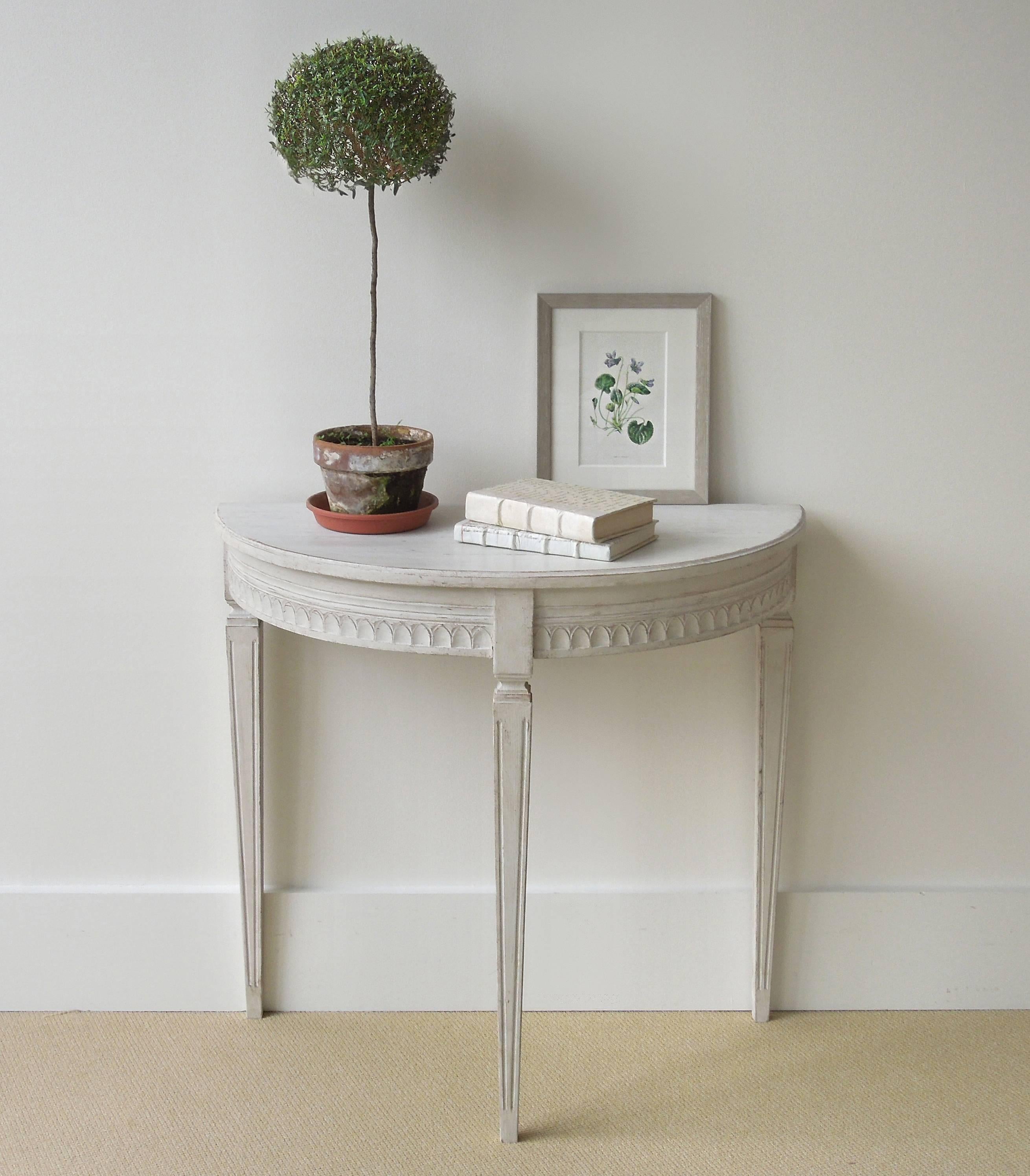 A hard to find pair of small Swedish painted demilune console tables with molded edge, leaf-tip carved apron, and tapered straight legs with fluting. Very elegant form. Hard to find in this small size.
