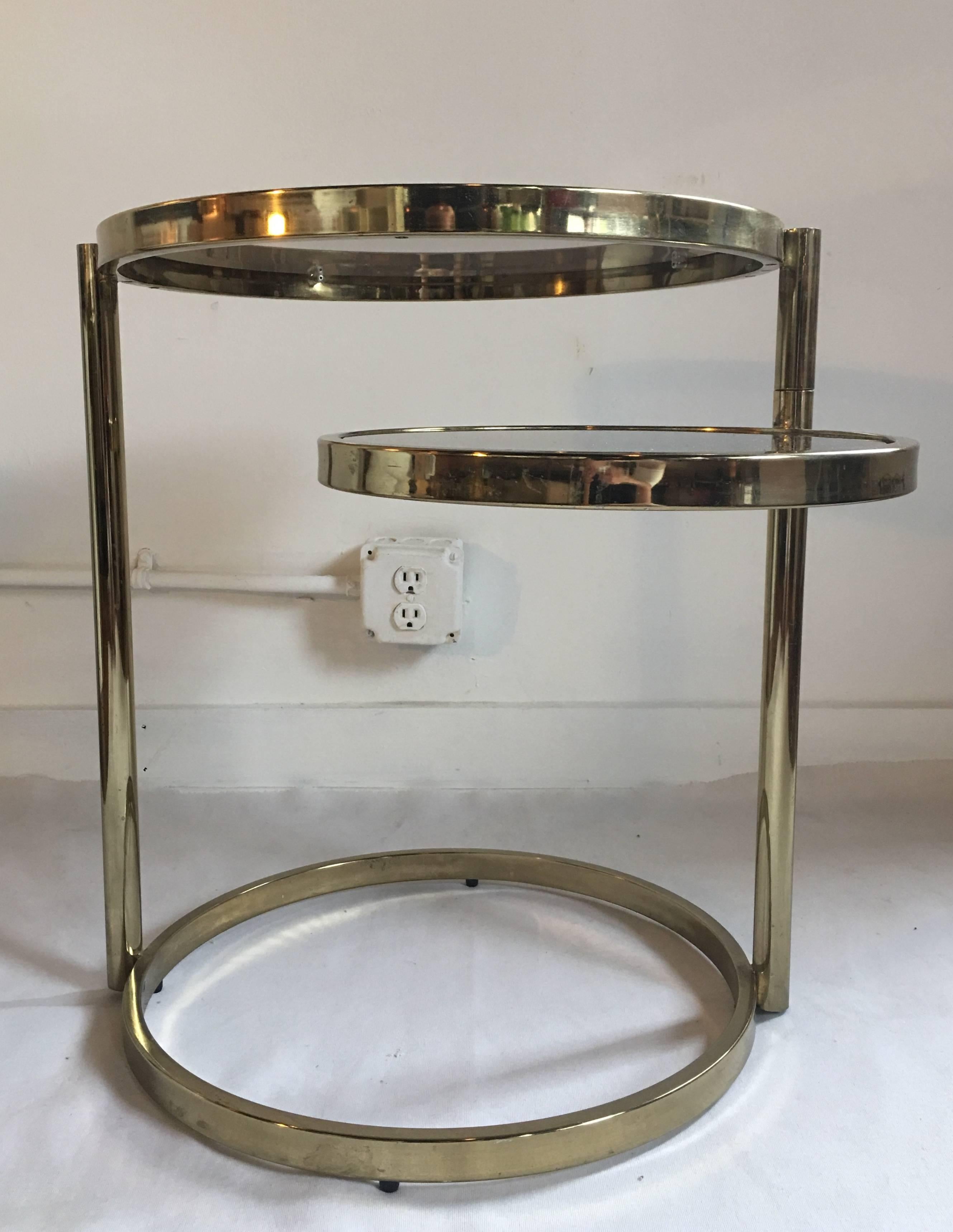 1970s Milo Baughman style Mid-Century Modern two-tier articulating swivel brass accent or side table. Tubular brass plated frame features two removable round smoked grey glass inserts. Top tier is stationary while the bottom tier can swivel to