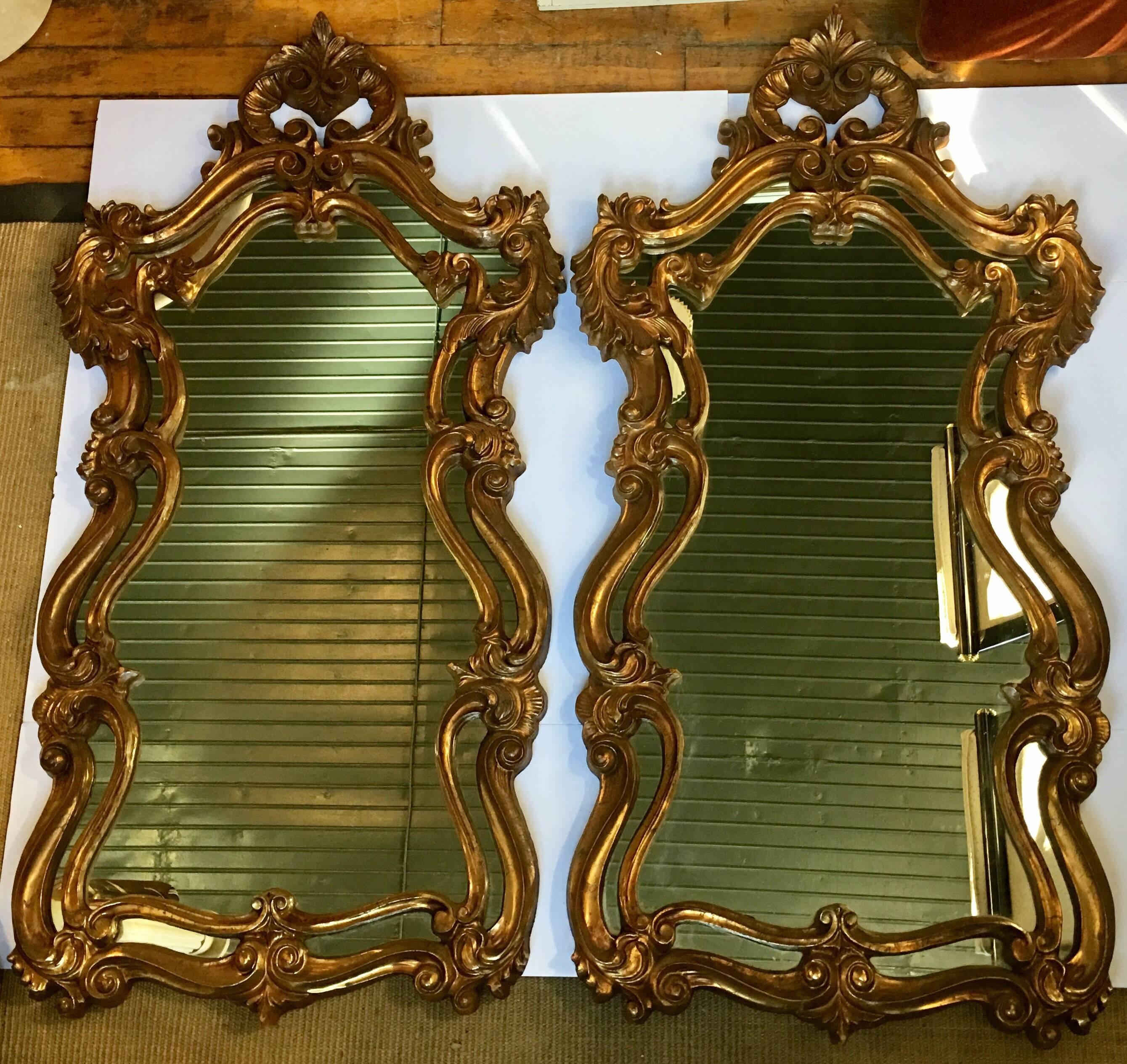 Large and impressive pair of Hollywood Regency style gold painted composition carved wood-like wall mirrors. These glamorous Rococo style mirrors feature pierced and foliate detailed frames. Could be displayed over a pair of consoles or matching