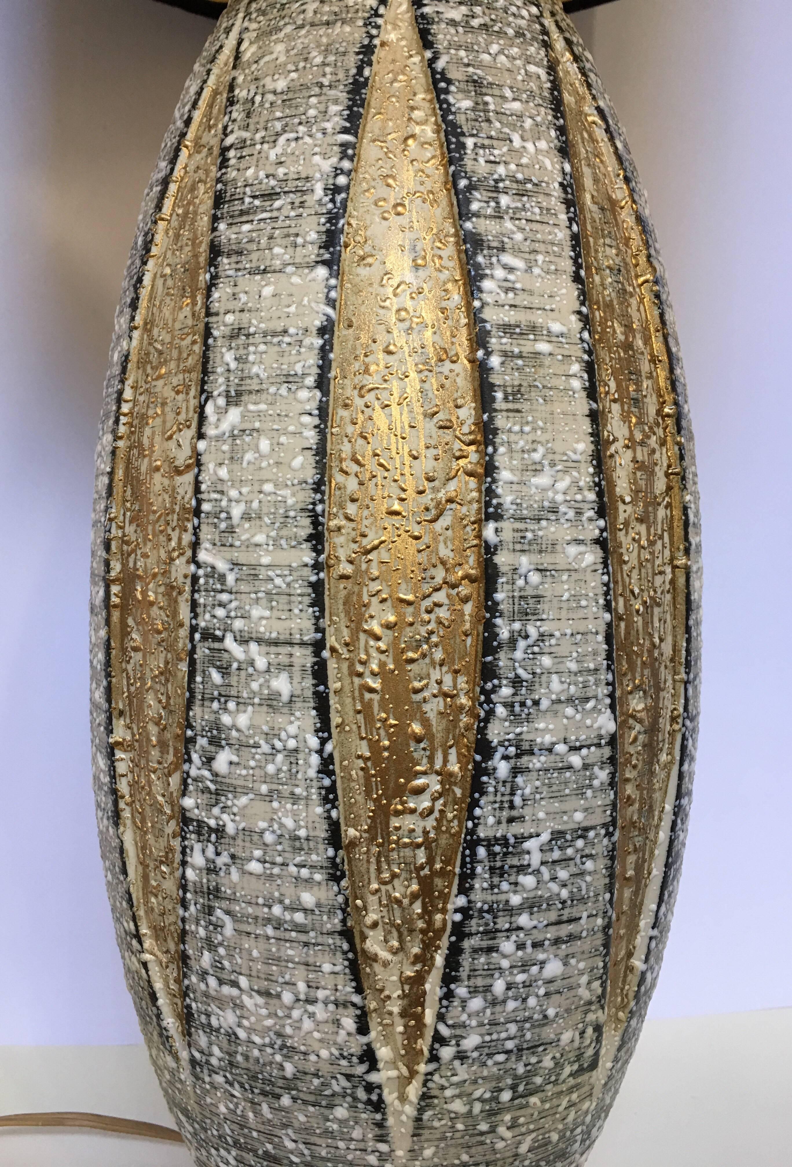 Mid-Century Modern Keramik Lava glasiert Tischlampe. Diese atomar inspirierte Lampe zeichnet sich durch ein dimensionales Blatt- oder Dart-Design mit goldfarbenen Metallic-Akzenten aus. In Anlehnung an Bitossi, Raymor und Guido Gambone.
Lampenschirm