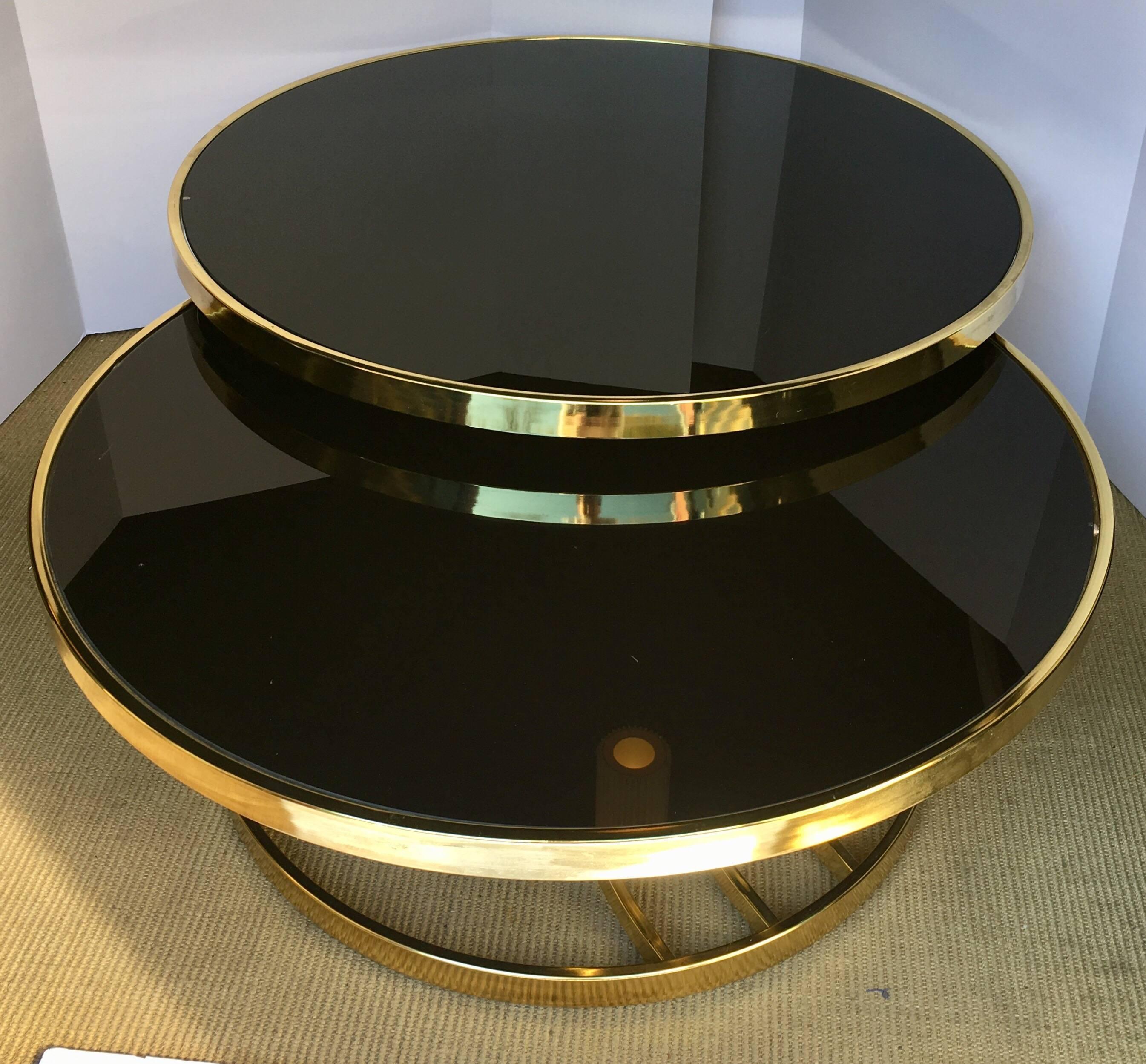 Mid-Century Modern round two-tier coffee table attributed to Design Institute America DIA. Brass plated frame features banded sides with two sculptural curved supports and black glass tops. Top tier is connected to a swivel mechanism and smoothly