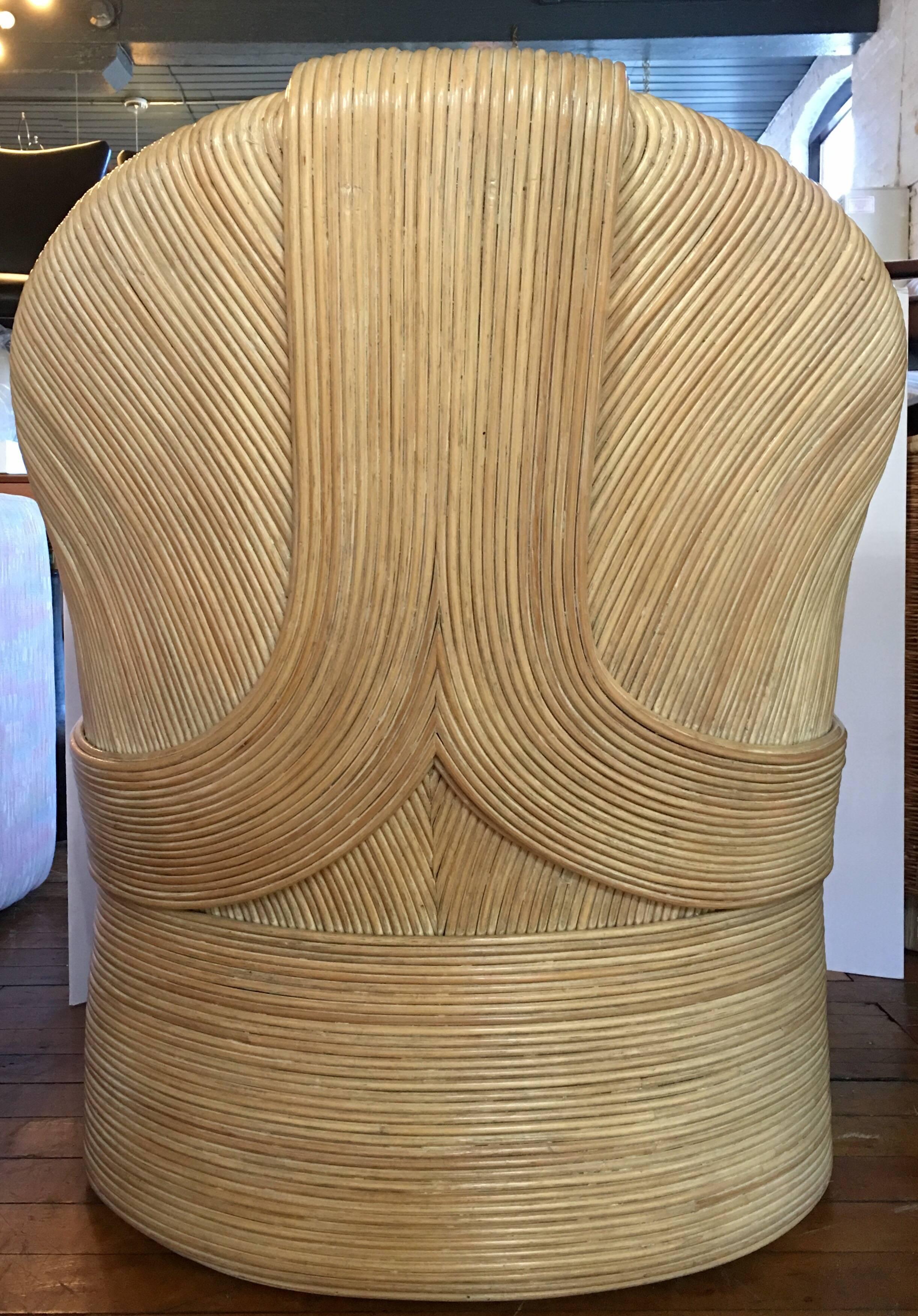 Sculptural curved Mid-Century Modern rattan lounge armchair in the style of Paul Frankl. Sturdy bamboo wicker frame features draped swag detailing with original removable back and seat cushions. Cushions can easily be reupholstered.
Measure: Seat