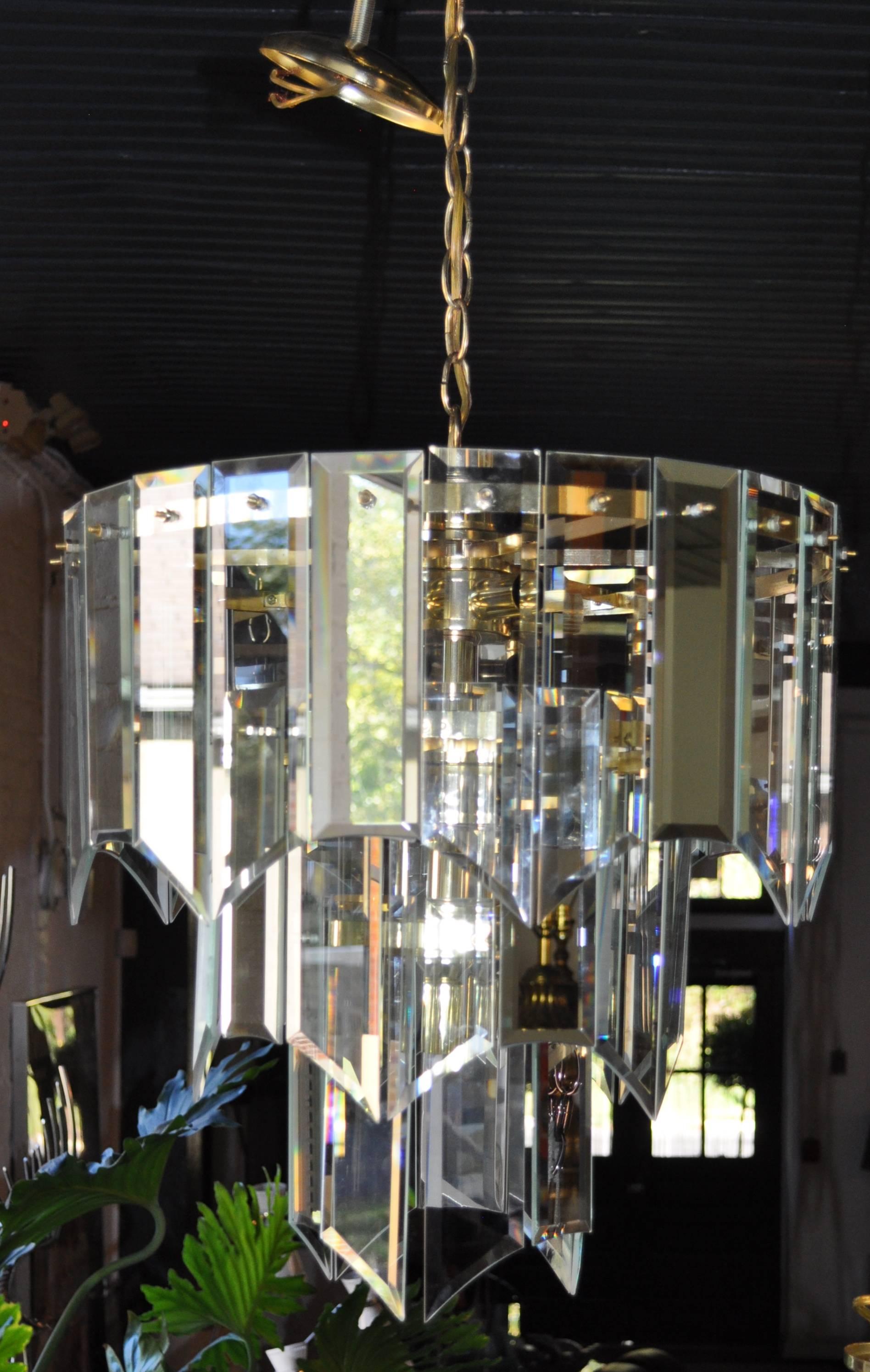 Mid-Century Modern waterfall chandelier featuring three tiers of arched/draped beveled clear glass prisms alternating with reflective mirrored glass prisms - all suspended from a brass frame.  
Canopy and 13 inches of brass chain included.  Nine
