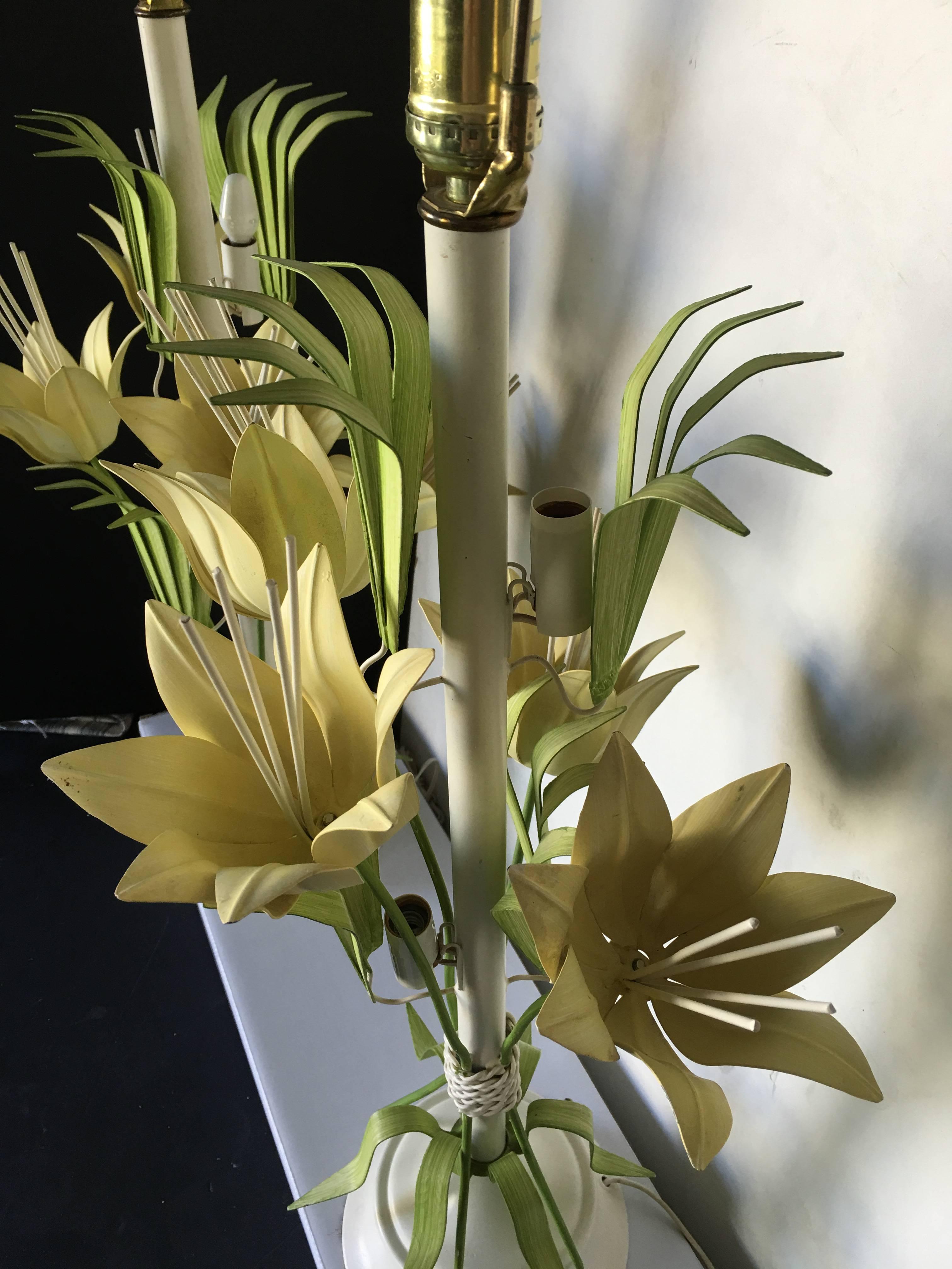 Charming pair of metal tole painted table lamps featuring a bouquet of flowers and tropical palm leaves. Standard bulb with two candle bulbs mounted within the base. Original wiring in working condition.
 