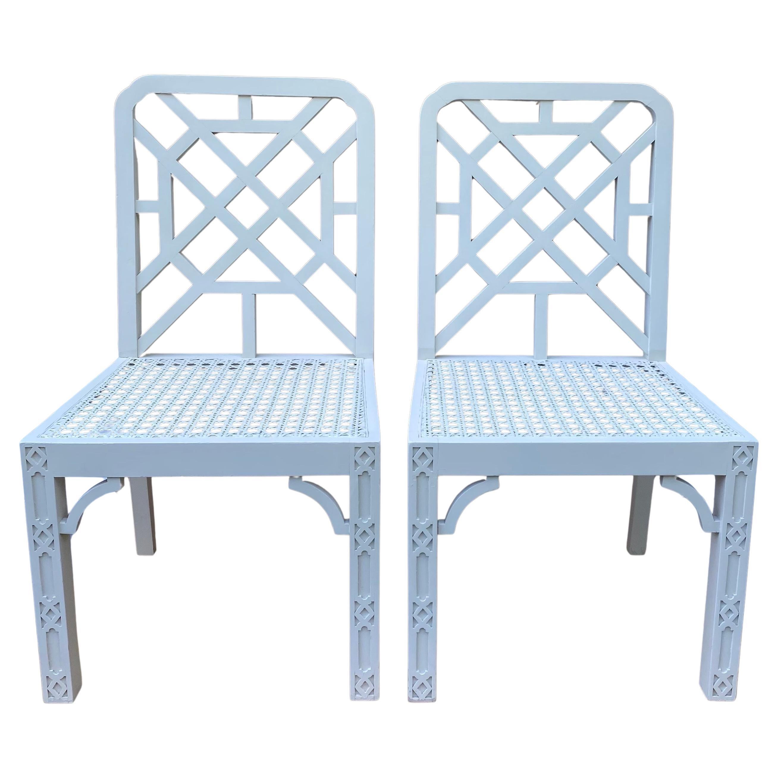 Set of two Chinese Chippendale style carved wood armchairs with cane seats.  These neutral cream painted side chairs feature beautifully pierced trellis backs and intricate fretwork detailing on the front legs.  These Chinoiserie style chairs are
