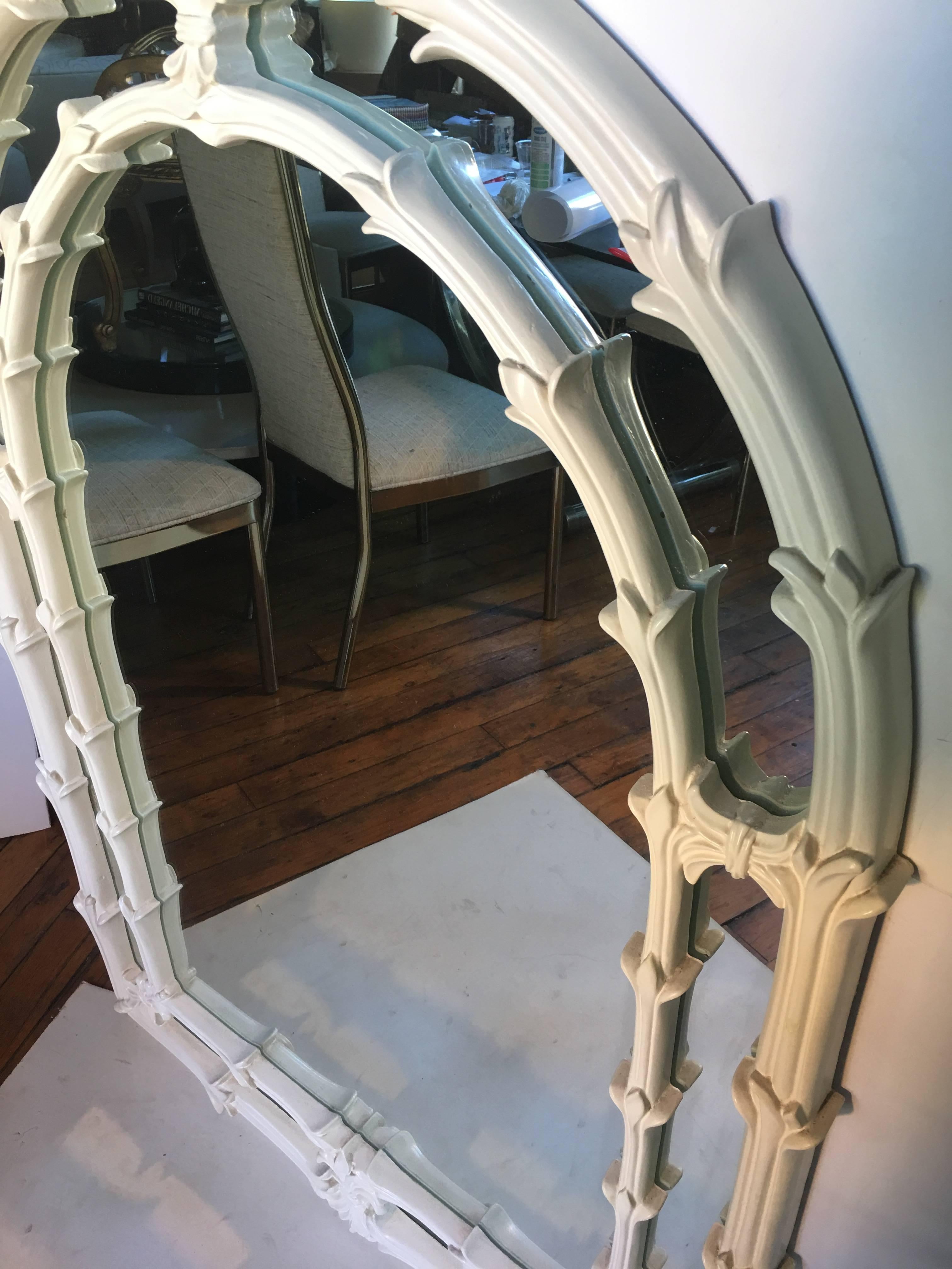 Large Hollywood Regency/ Palm Regency style arched wall mirror in the style of Serge Roche. Matte cream painted plaster-like wood frame features carved foliate details.
 