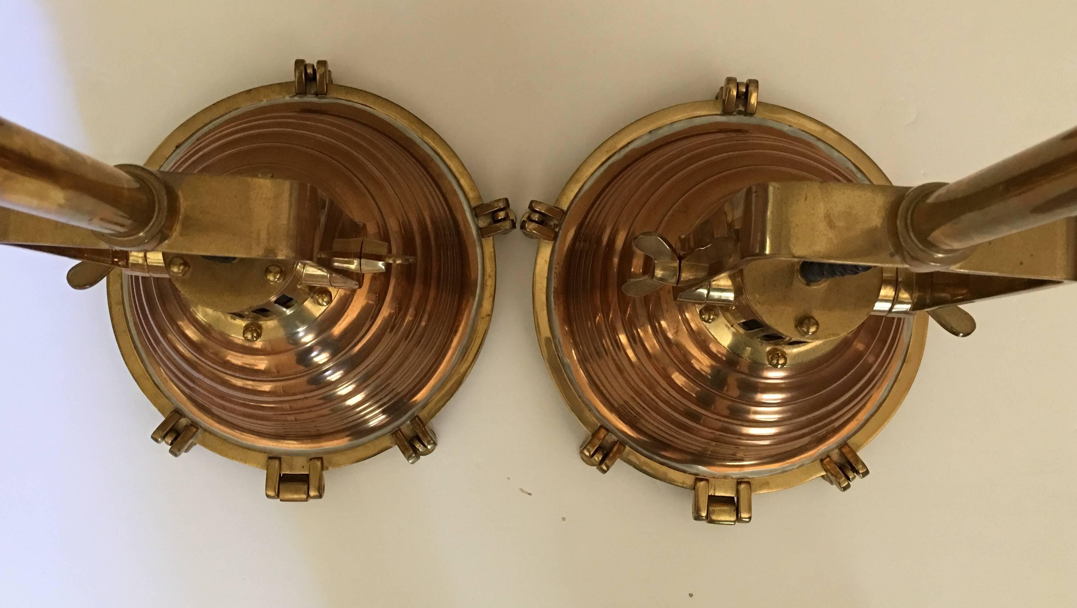 Pair of large polished copper and brass pendant lights by Luminaire.  Suspended from tubular brass rods, the adjustable heads feature white glass lenses which unscrew to access concealed bulb. Original wiring in working condition.