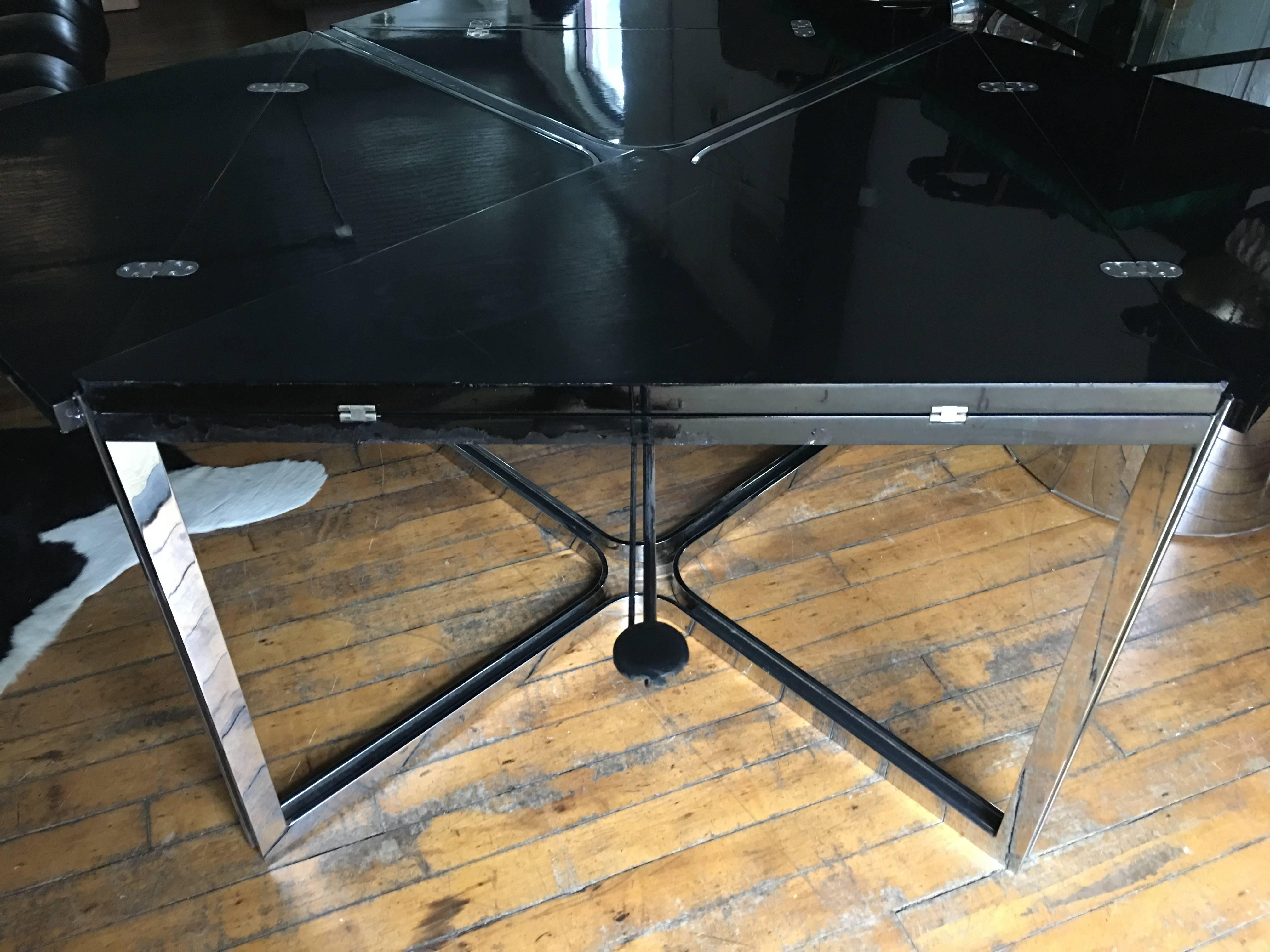 Mid-Century Modern flip-top square dining or game table in the style of Drylund. 
Polished chromed steel frame with black lacquer wood top. Four pullout support arms can be extended for additional support when table is unfolded. 
Table measures