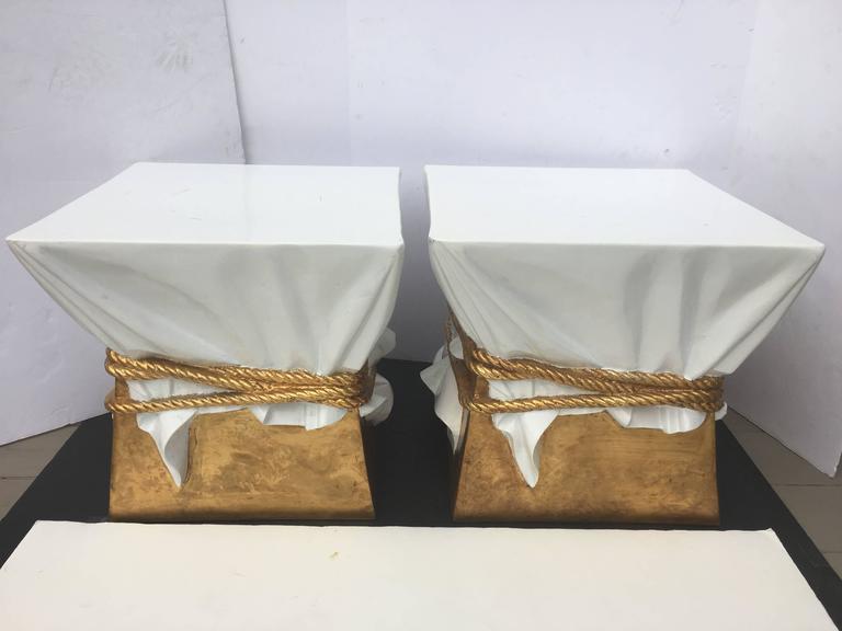 Mid-Century Modern Italian or French lacquer faux draped side or end tables featuring original gilt painted roped detailing on all four sides. Surrealist stools feature white lacquered draped form fabric with gold roping and base. Pair can be